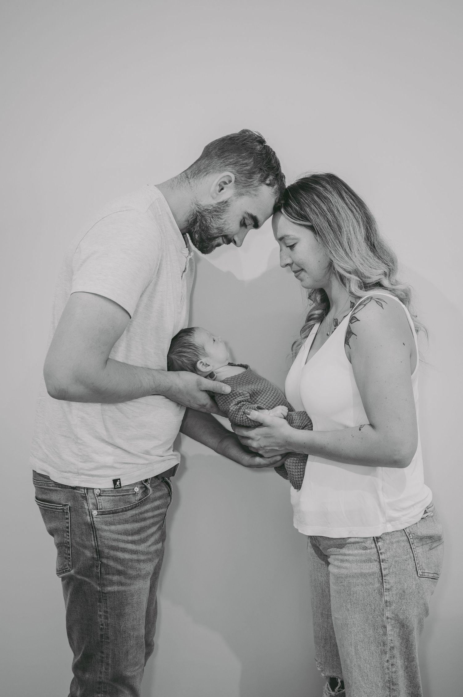 Black and white portrait of parents gazing lovingly at their newborn baby.