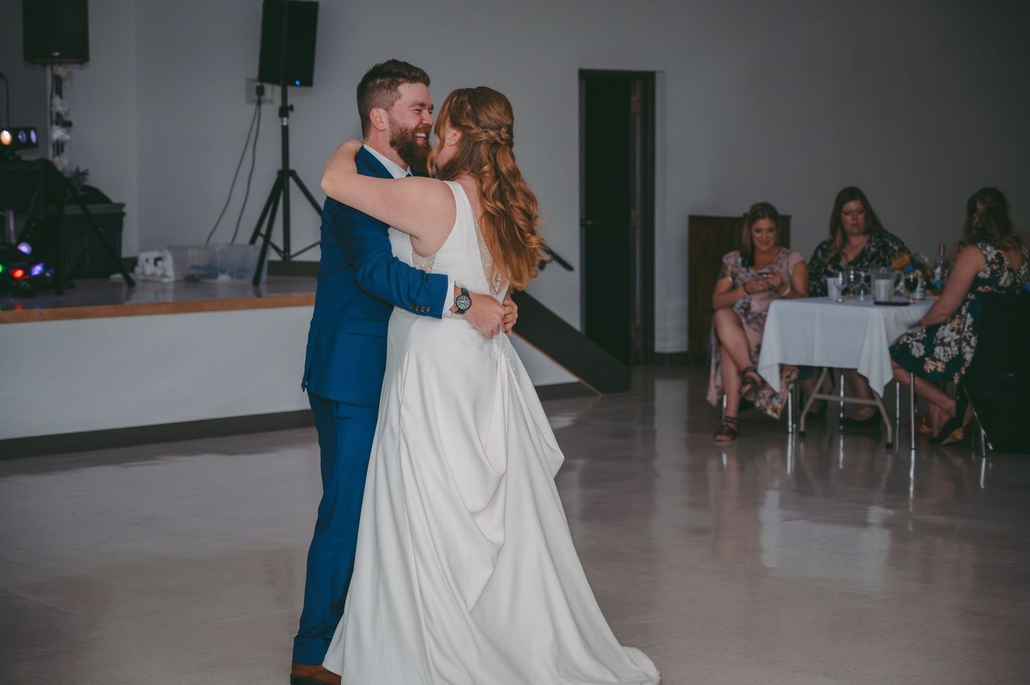 Couple shares their first dance at wedding reception in a bright venue with guests watching.