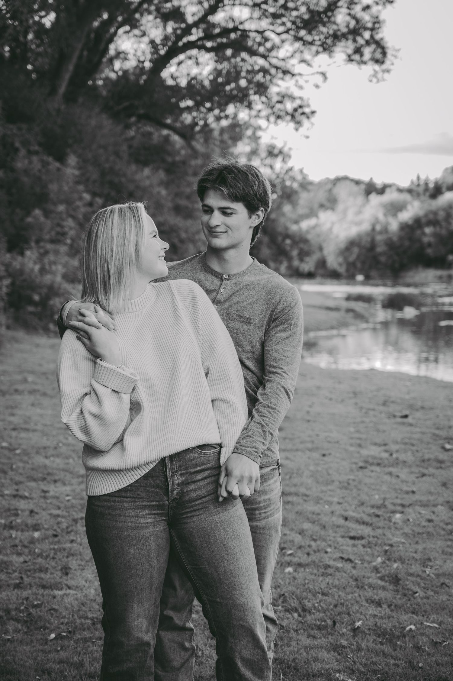 A couple in casual attire sharing a romantic moment by a lake in black and white.