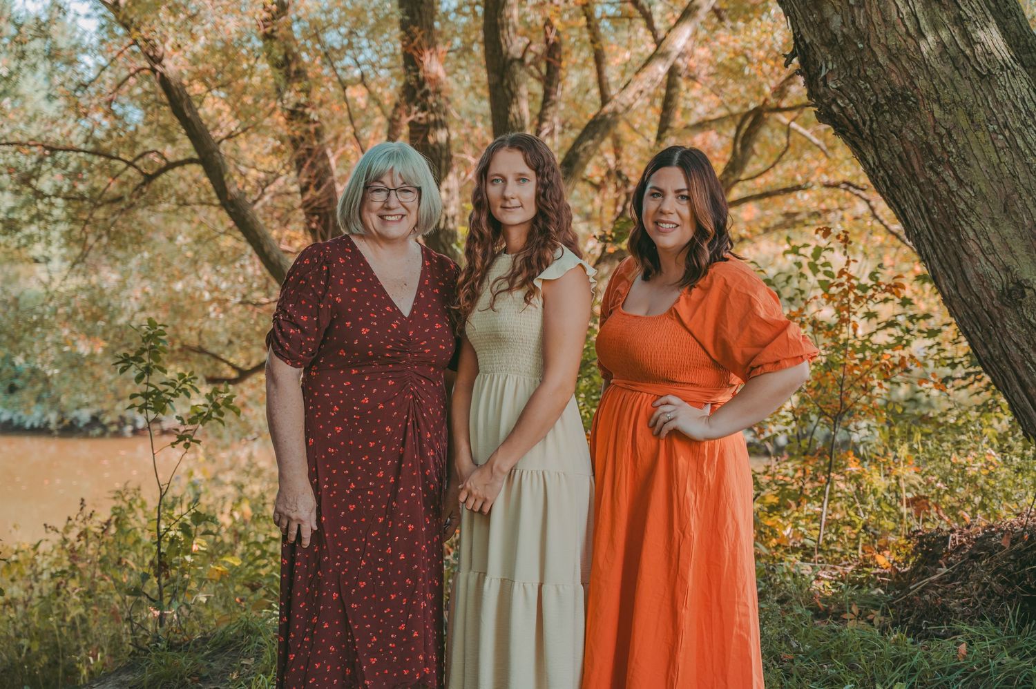 Group photo of women in coordinated dresses standing beneath fall foliage.