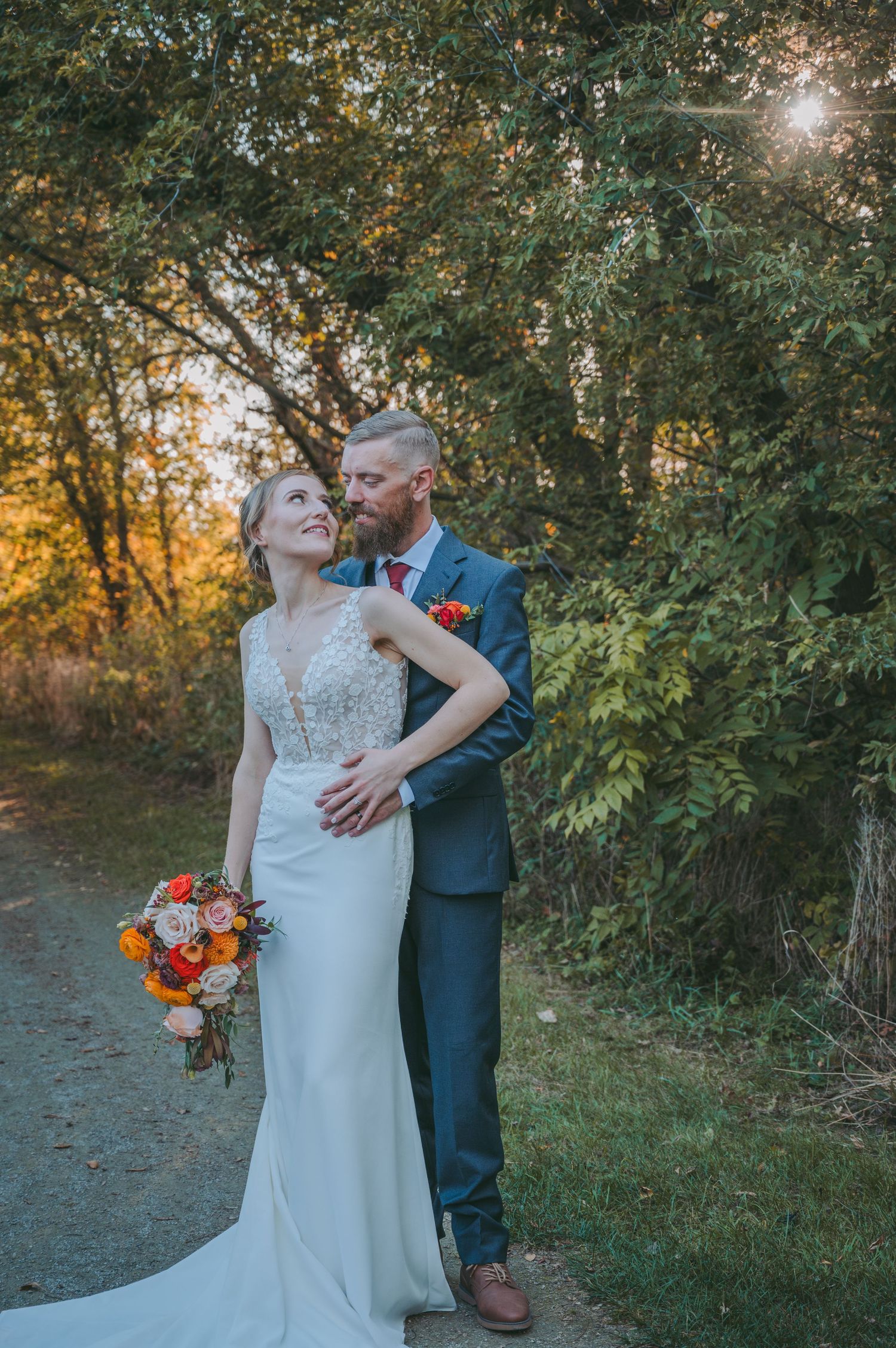 A romantic sunset wedding portrait with the couple embracing among autumn trees.