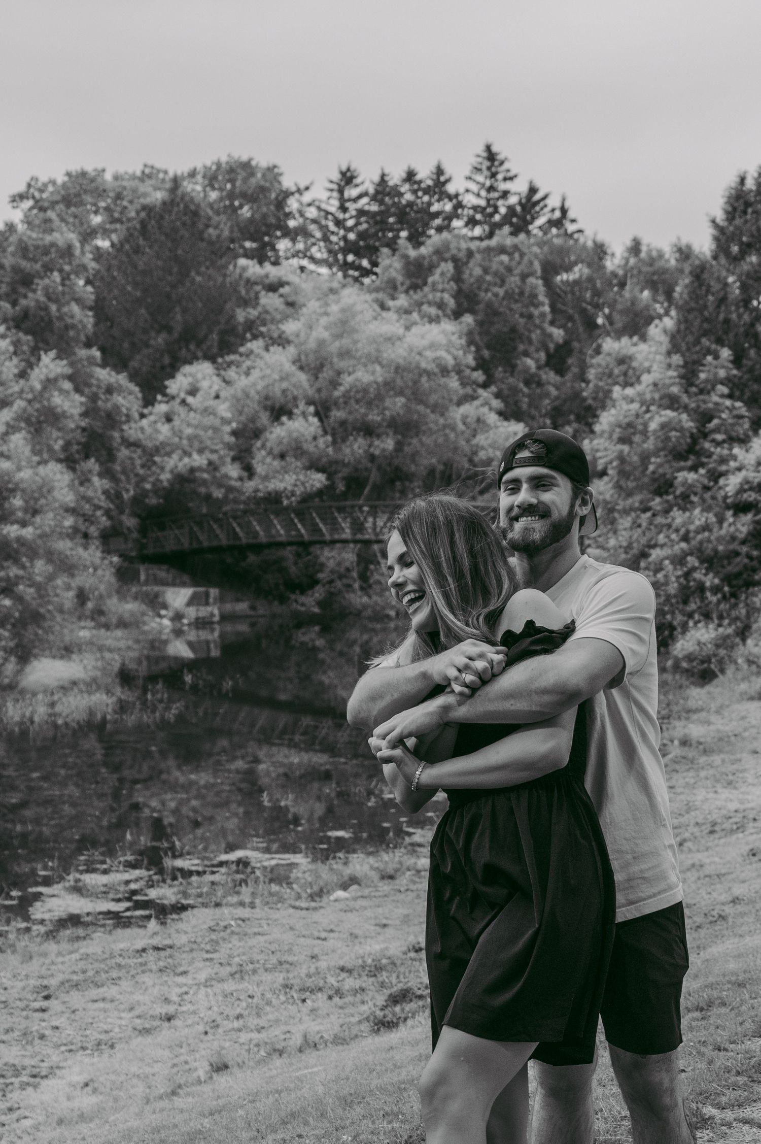 A couple embraces and laughs together in a casual outdoor photoshoot with trees in the background in black and white in Listowel.
