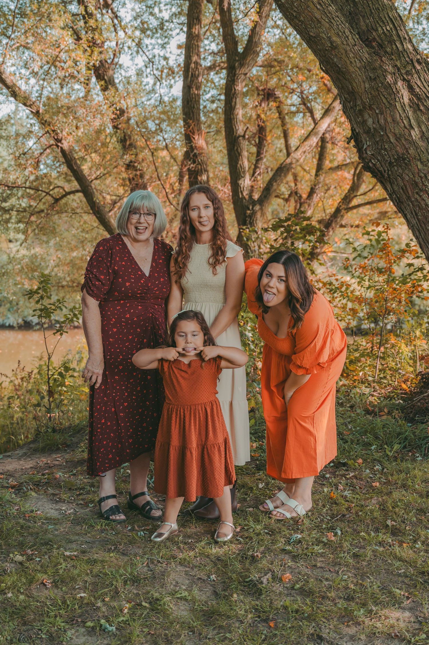 Ladies in coordinating orange and burgundy dresses pose together against autumn trees.