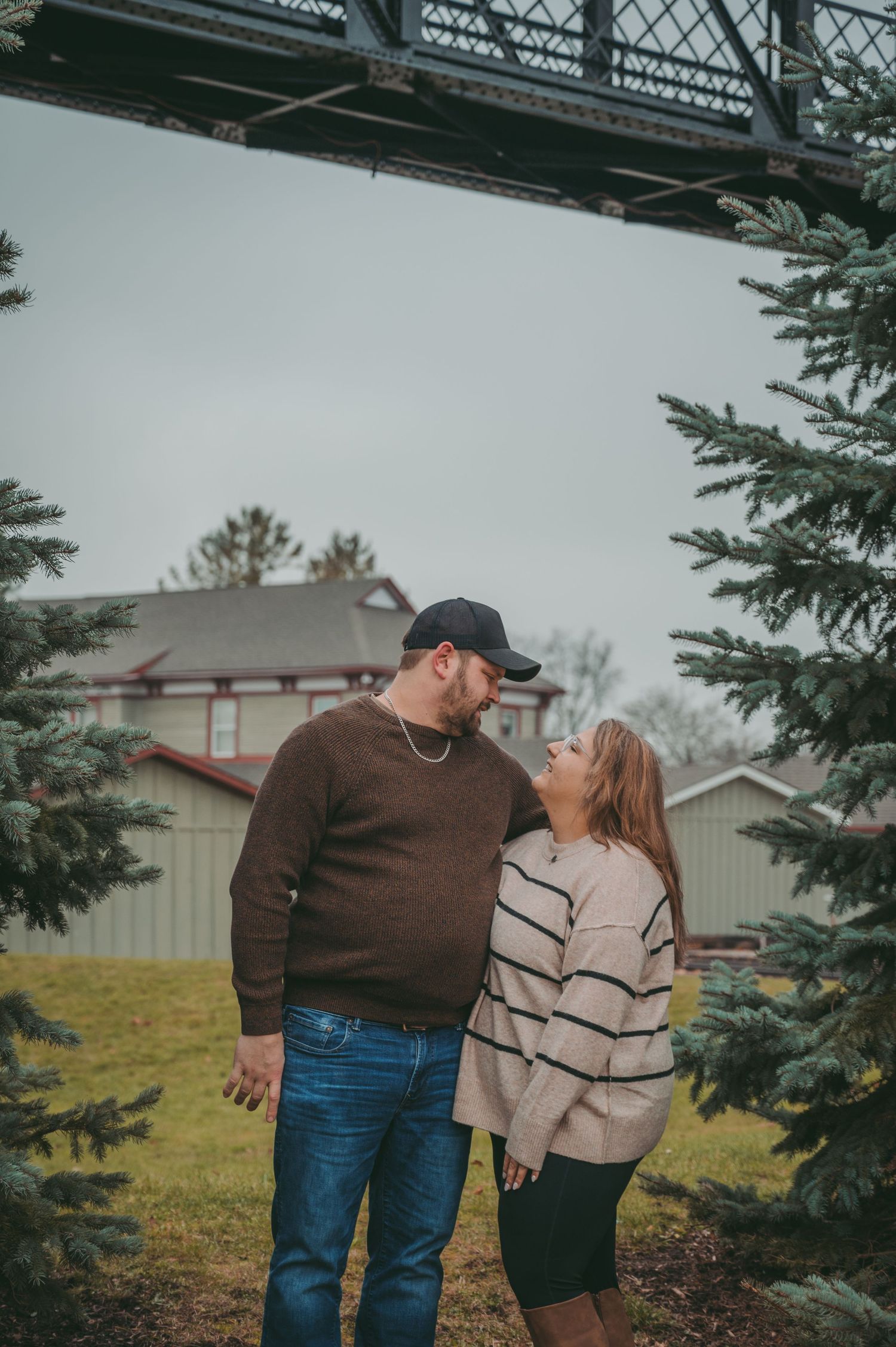 Couple sharing a playful moment under a metal bridge structure during an overcast day.