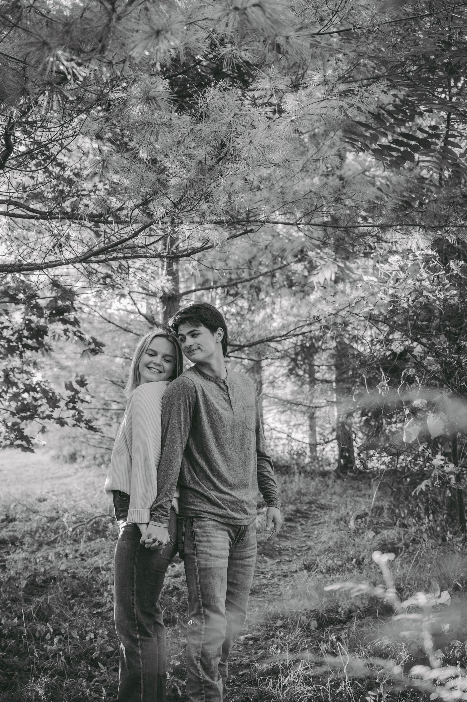 A black and white portrait of a couple sharing an intimate moment in a wooded setting.