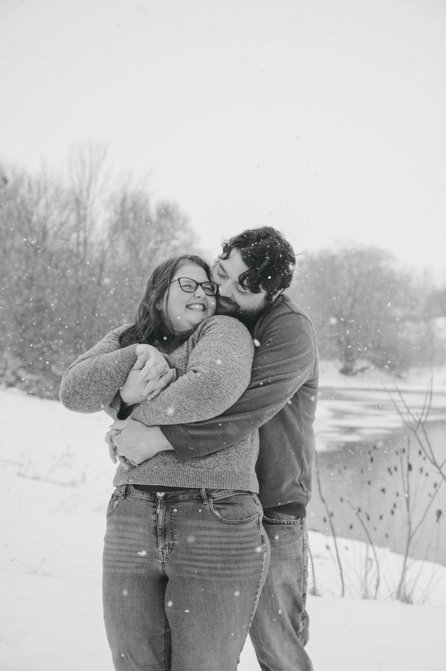 An affectionate black and white portrait of a couple embracing during snowfall.