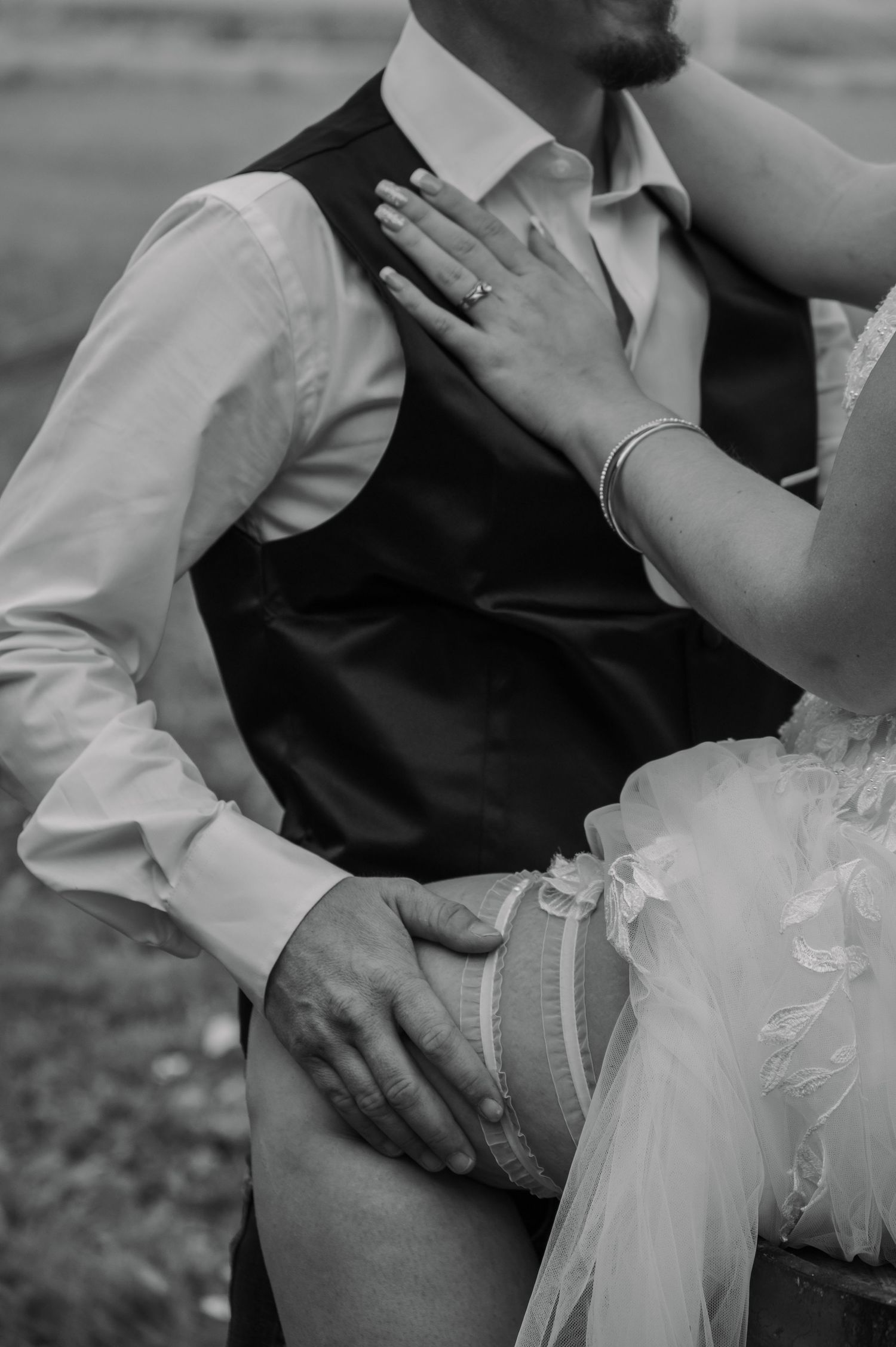 Black and white intimate wedding photo showing delicate hand placement and details of formal attire with veil and vest.