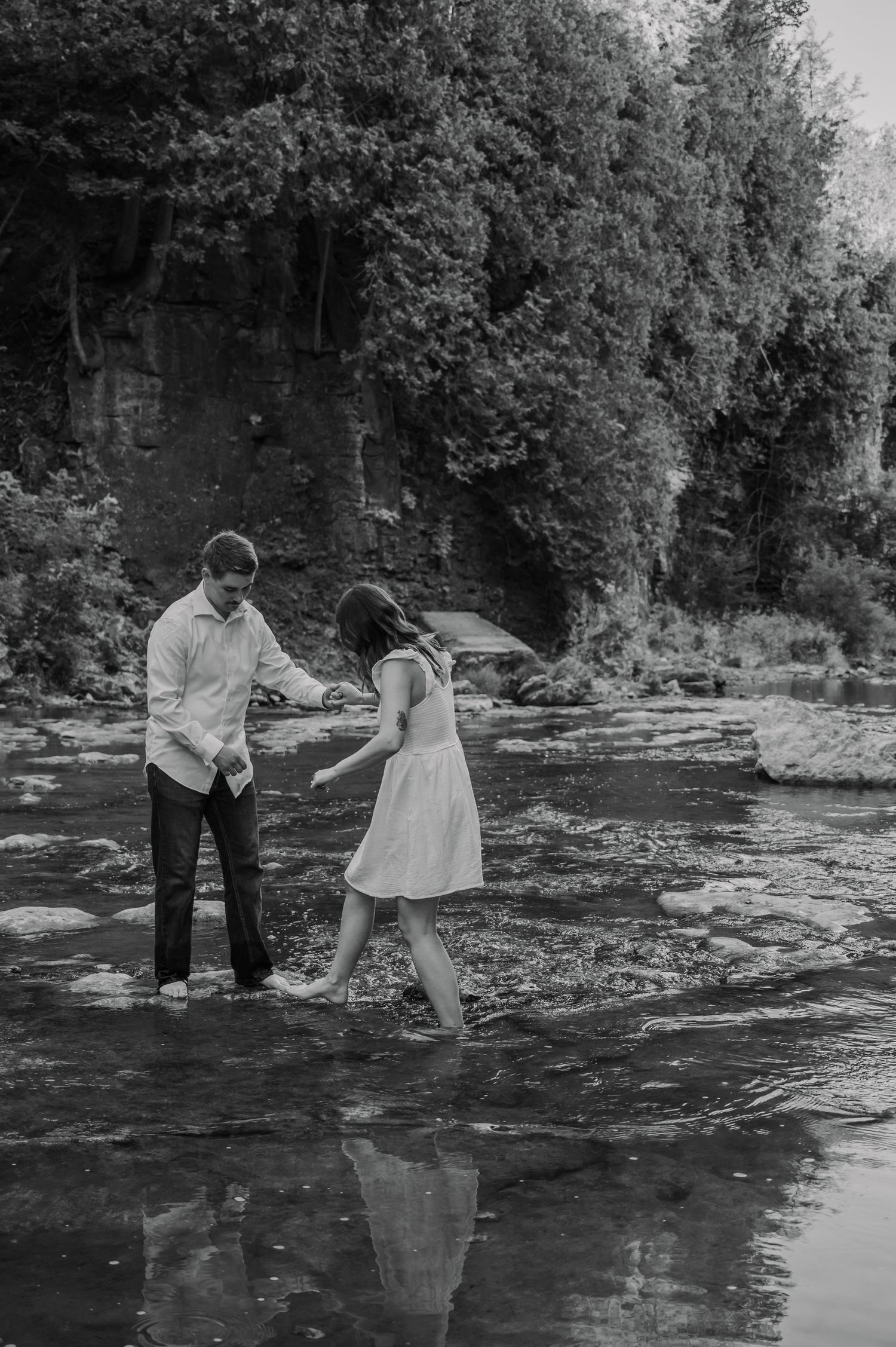 A couple explores a rocky riverbed together in a black and white photograph showing playful interaction at the Elora Gorge.