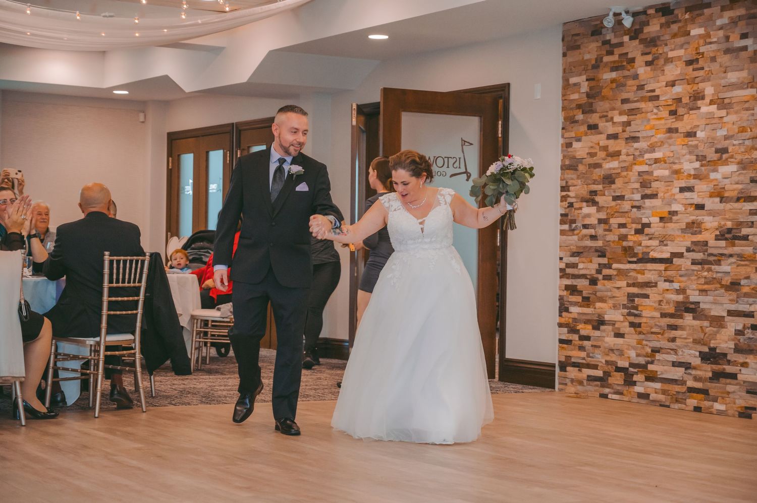 Wedding couple making their entrance into reception venue with stone accent wall.