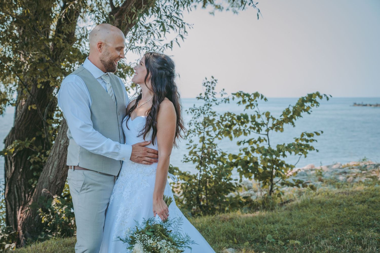 A couple poses for a romantic wedding photo with a scenic lake view in the background.