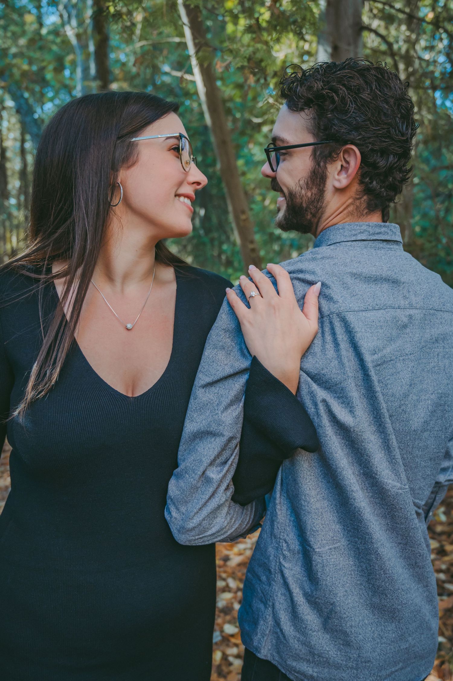 A joyful couple in casual attire sharing a tender moment among trees in a forest setting.