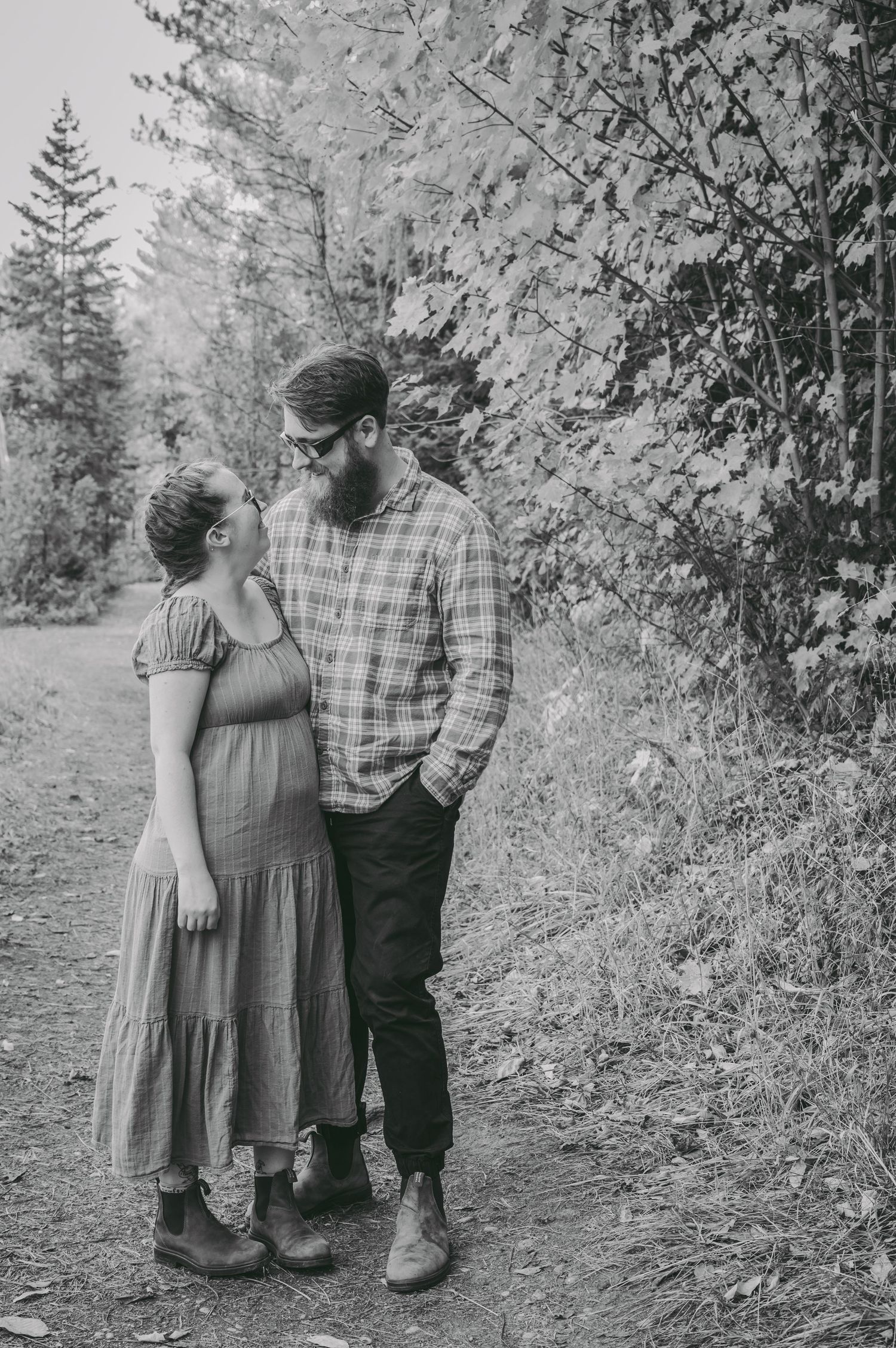 A romantic couple embraces on a forest path in black and white photography.