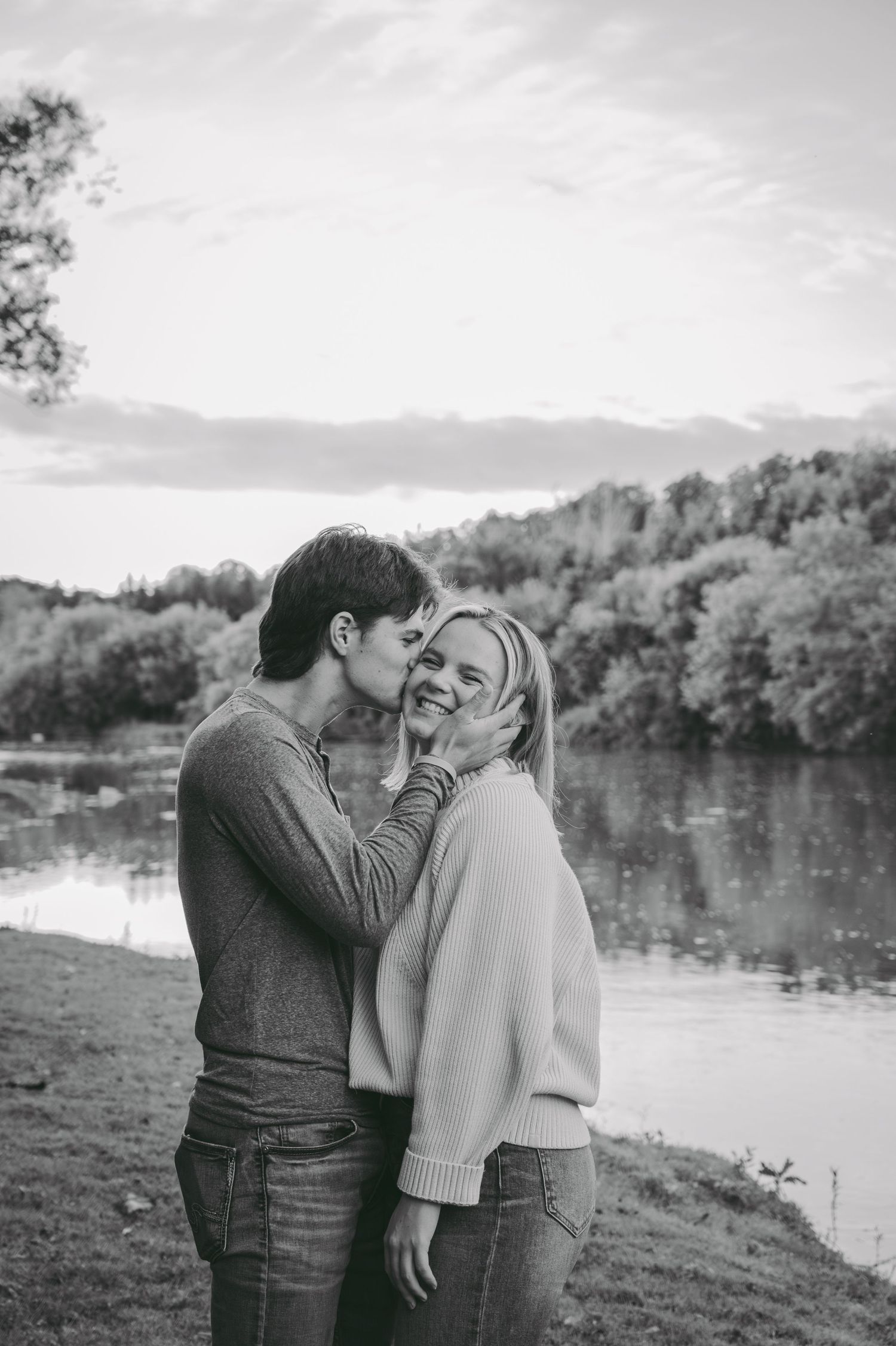 A tender moment between a couple by a lake with mountains and trees in the background.