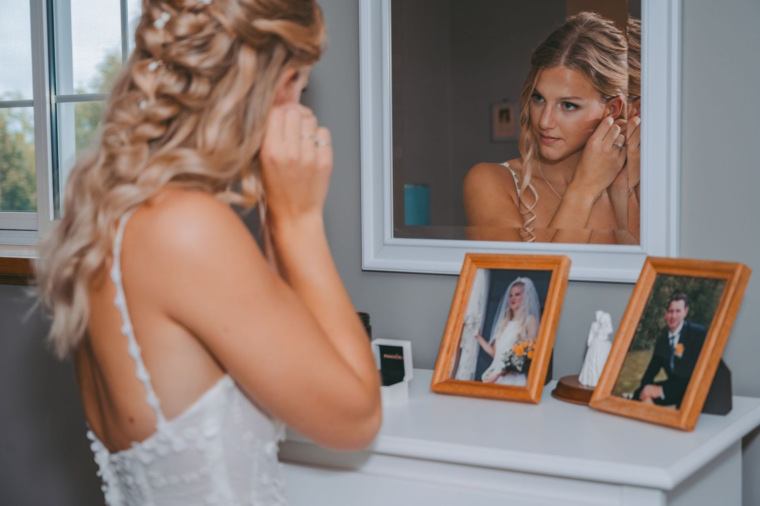 Bride getting ready in white dress looking at framed photos on vanity.