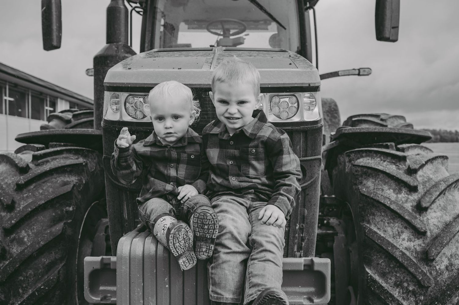 Two young children sitting together on the front of a large green tractor.