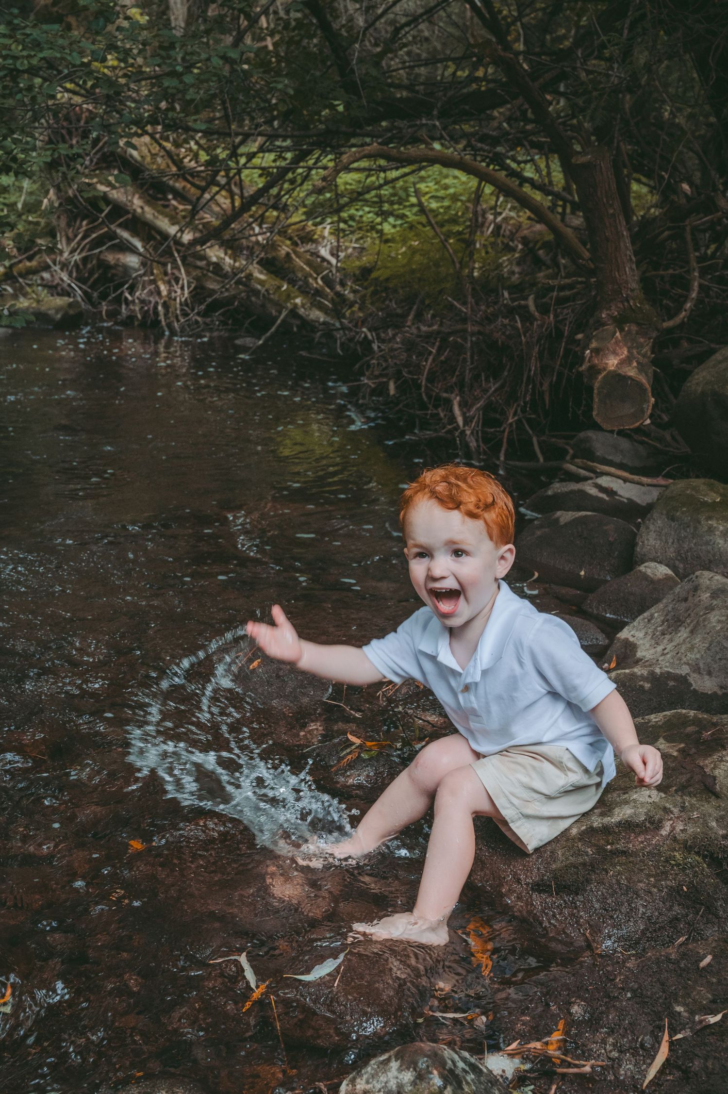 Young child playing in a stream while sitting on rocks.