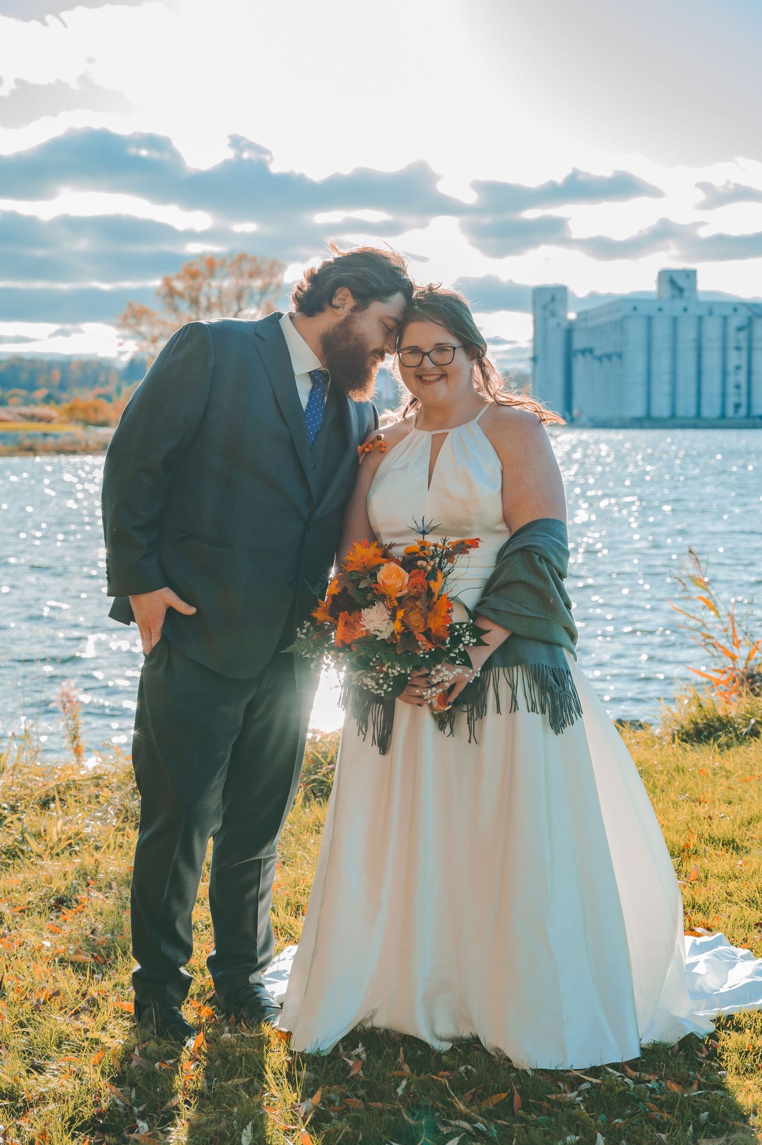 A waterfront wedding portrait with autumn colors and industrial buildings creating a unique backdrop.