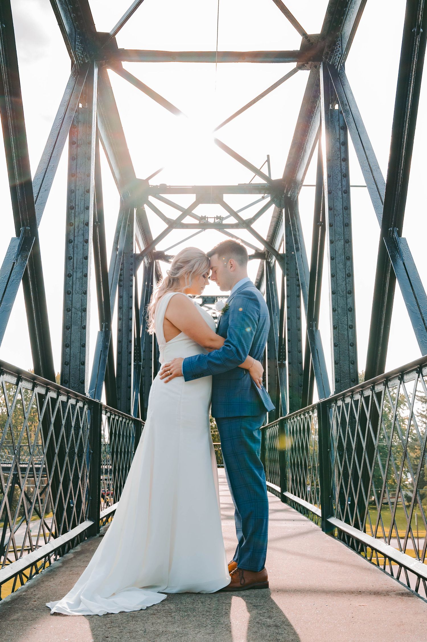 A romantic moment captured on a metal bridge with sunlight streaming through the structure.