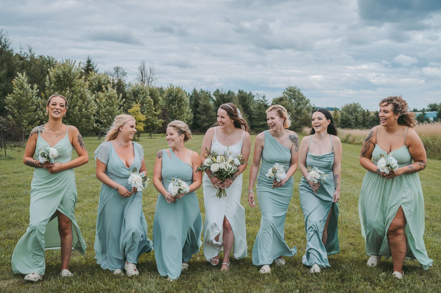 Bridal party in seafoam green dresses laughing together in an outdoor setting.