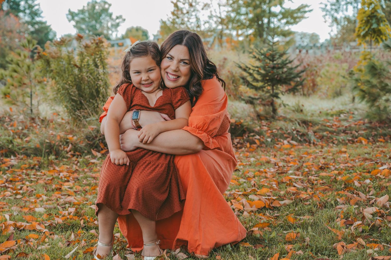 Family members in autumn clothing embrace on fallen leaves during a colorful outdoor photoshoot.