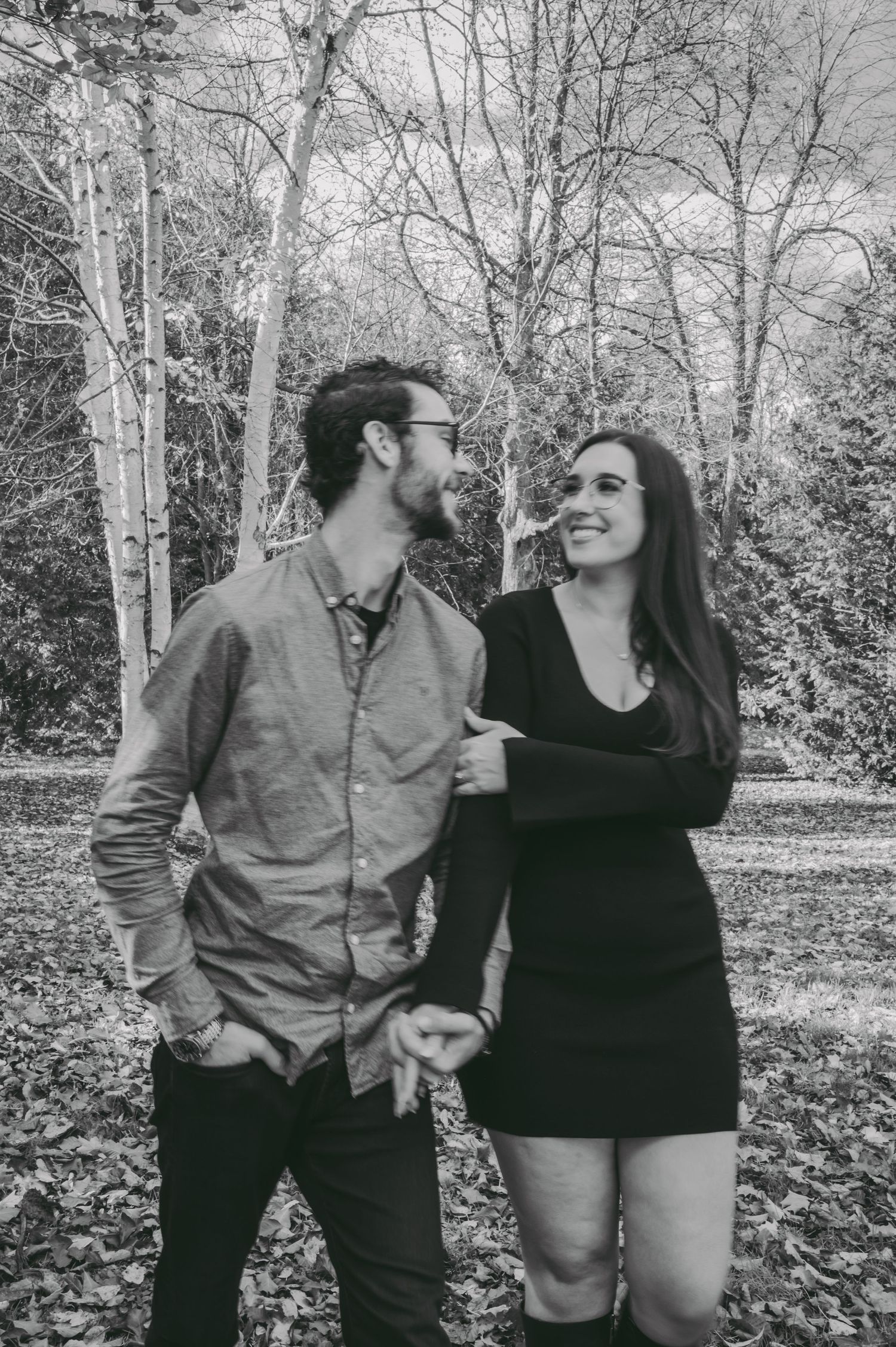 A black and white portrait of a couple laughing together in a wooded setting.