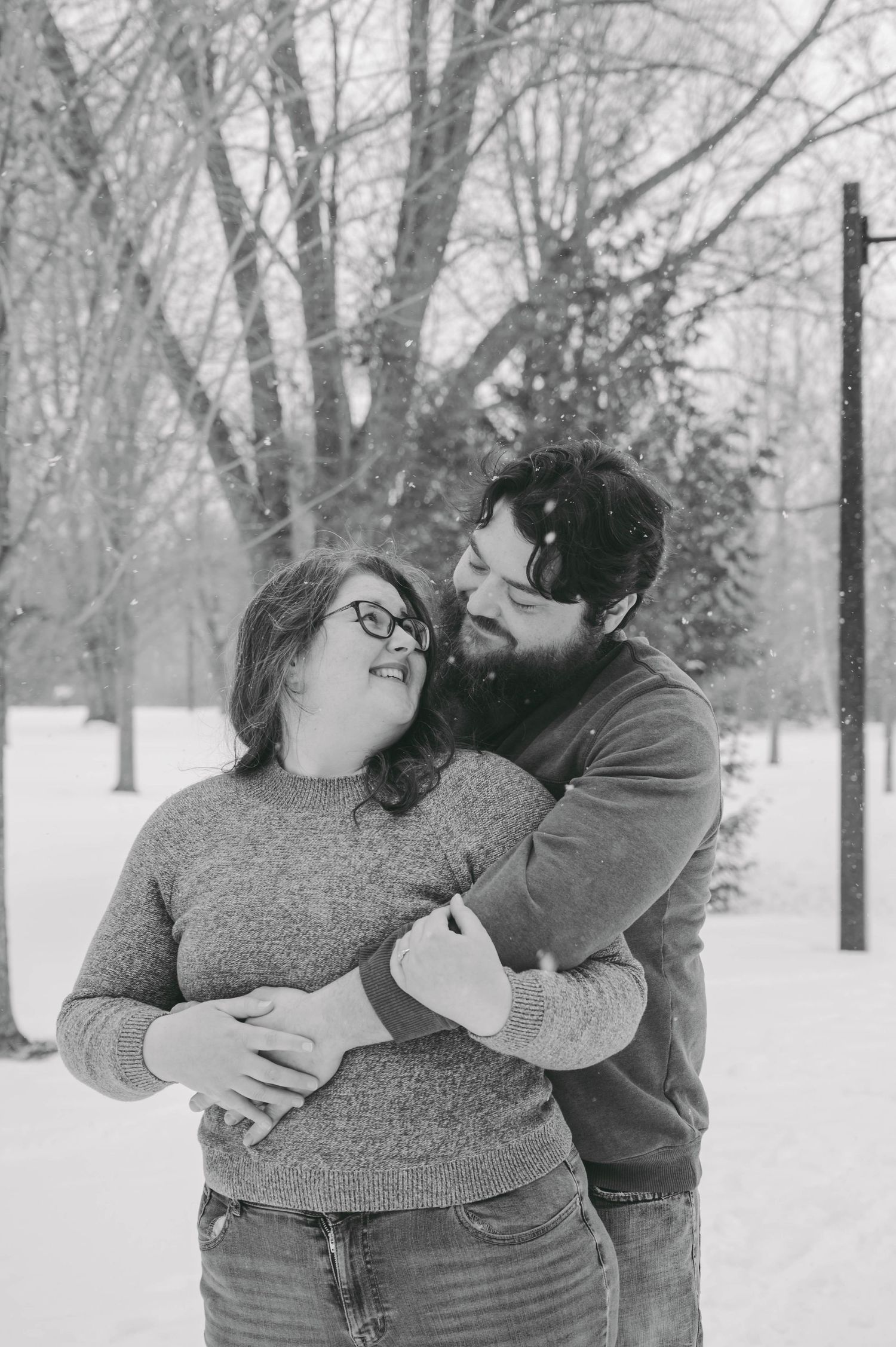 A tender black and white winter portrait of a couple sharing a loving embrace in the snow.