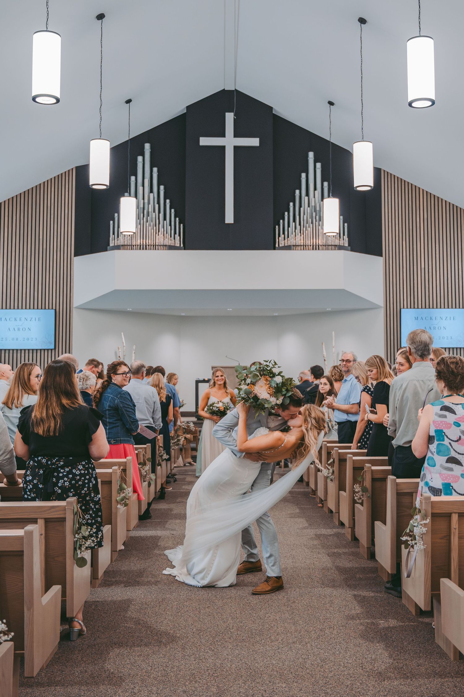 Modern church interior with wooden pews and dramatic black accent wall during wedding ceremony.