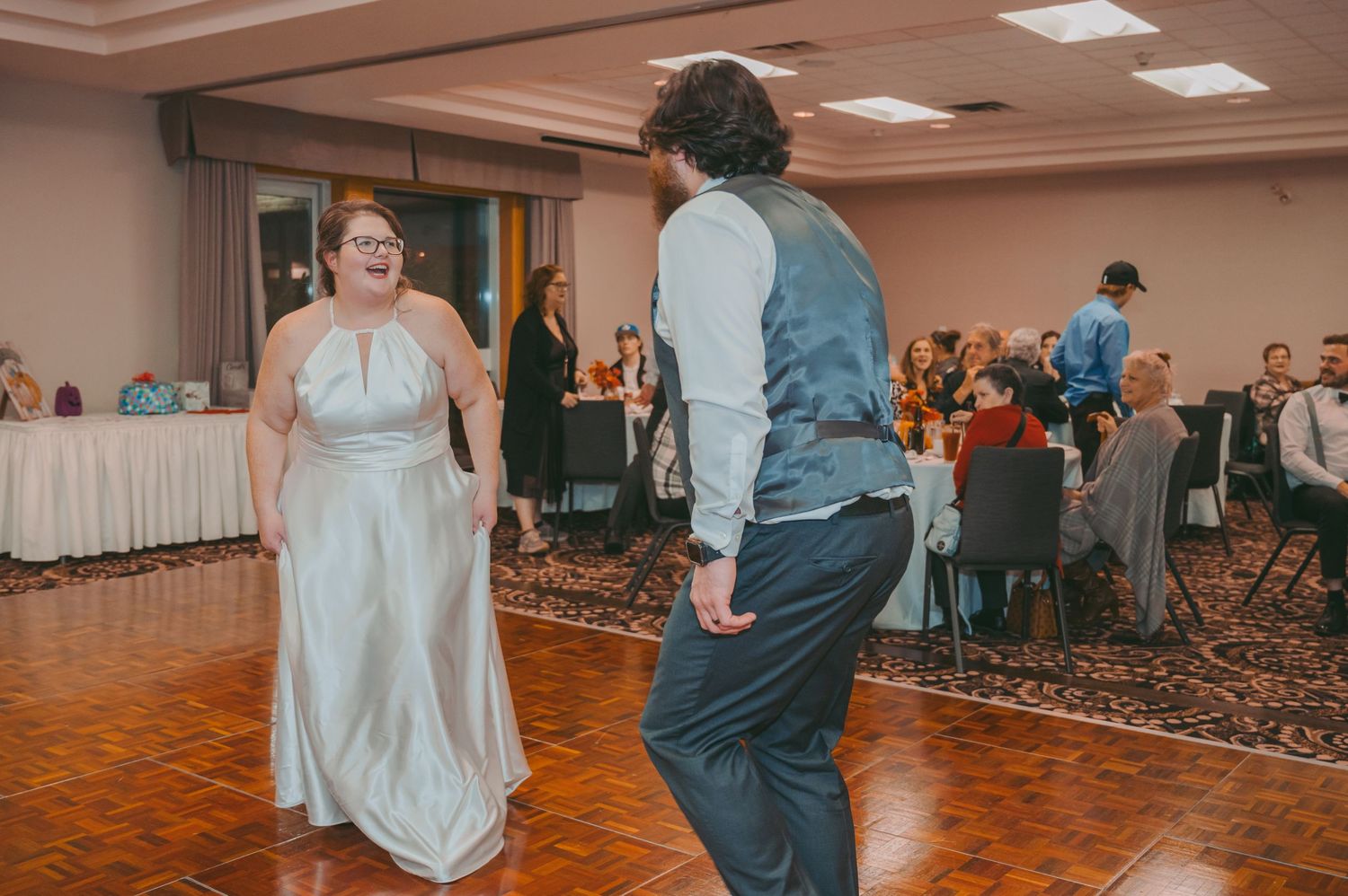 A couple shares a dance at their wedding reception surrounded by guests on a patterned carpet floor.