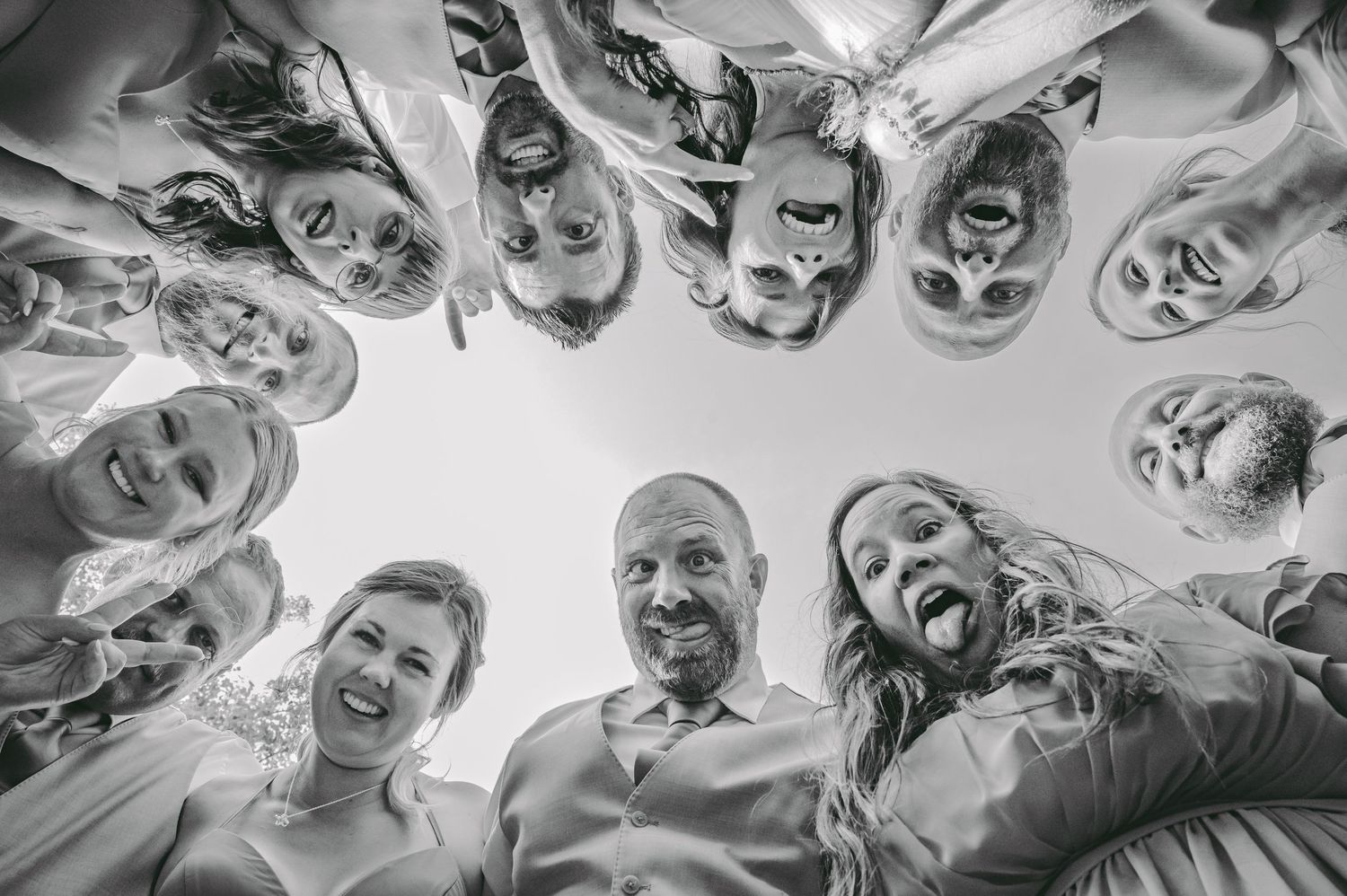 Black and white circular photo of wedding party looking down at camera with joyful expressions.
