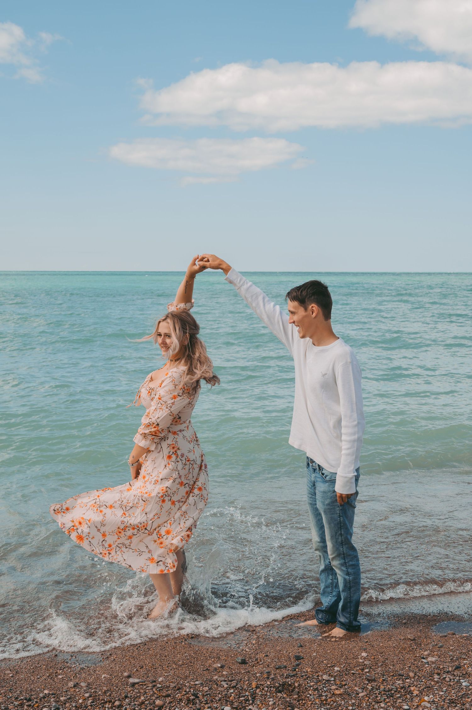 Dancing on beach shoreline as waves lap at feet with dress twirling in motion.