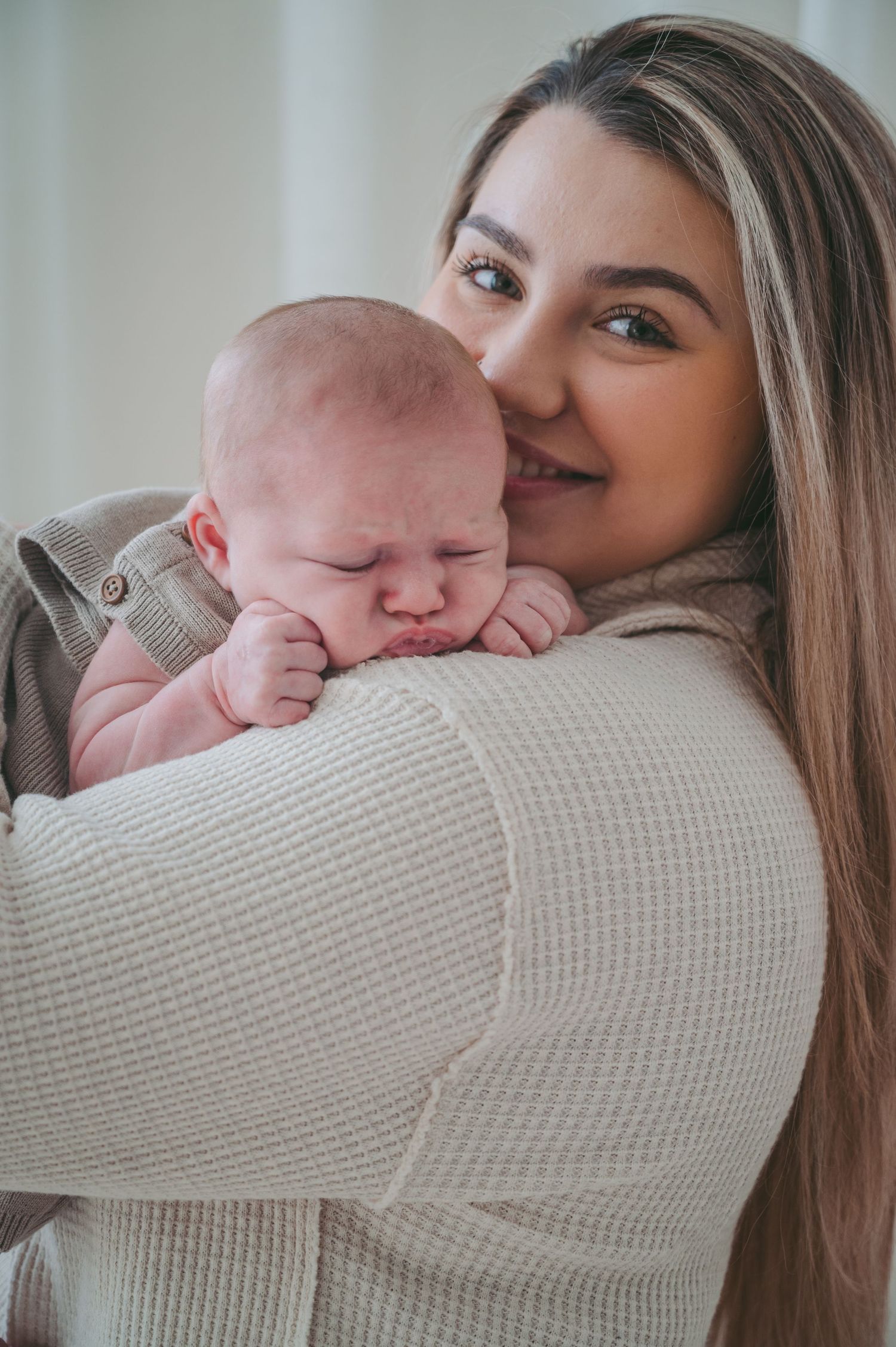 Sweet moment of cuddling with sleeping newborn against cream knit sweater.