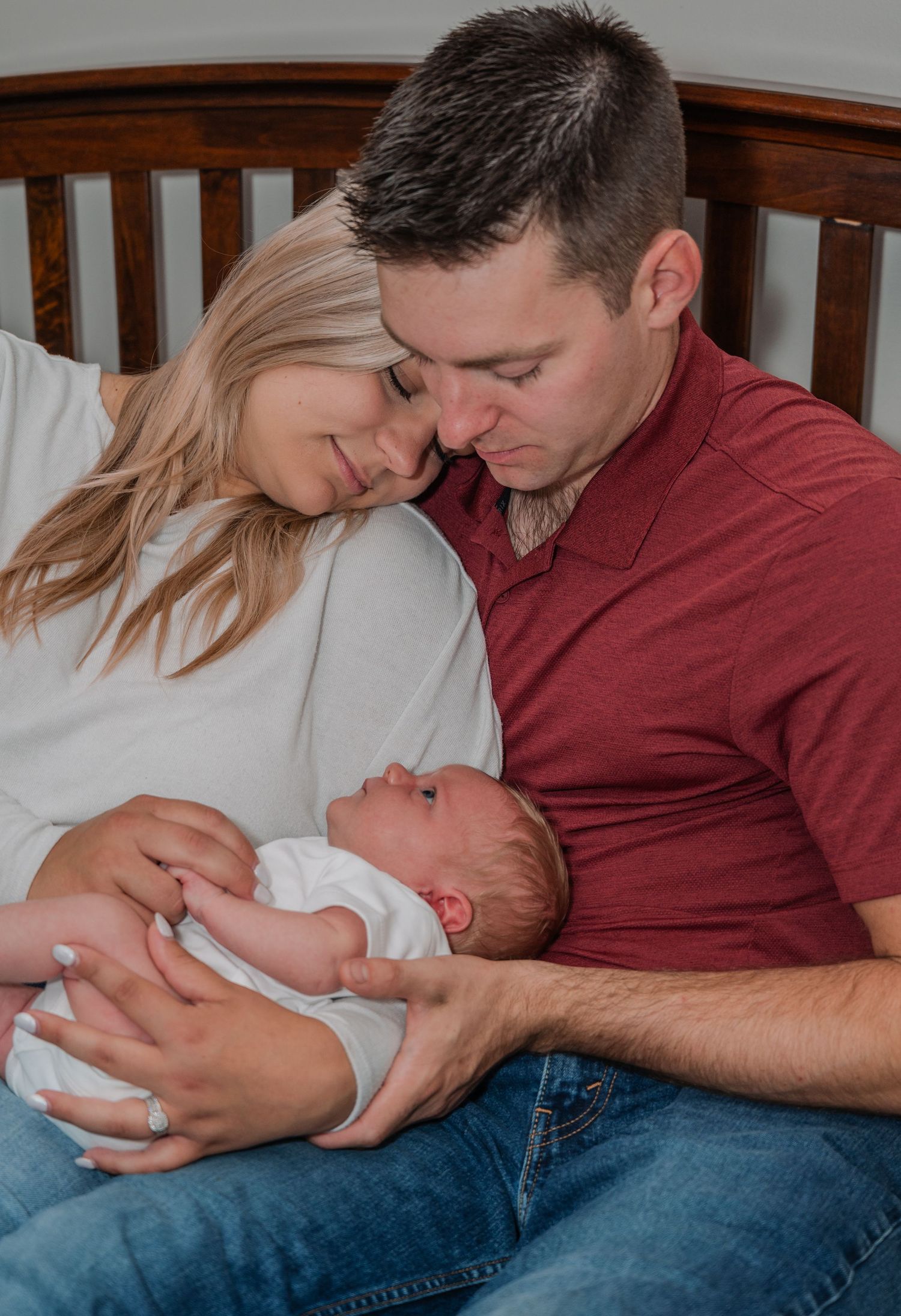 New parents lovingly cuddling and bonding with their newborn baby wrapped in white swaddle.
