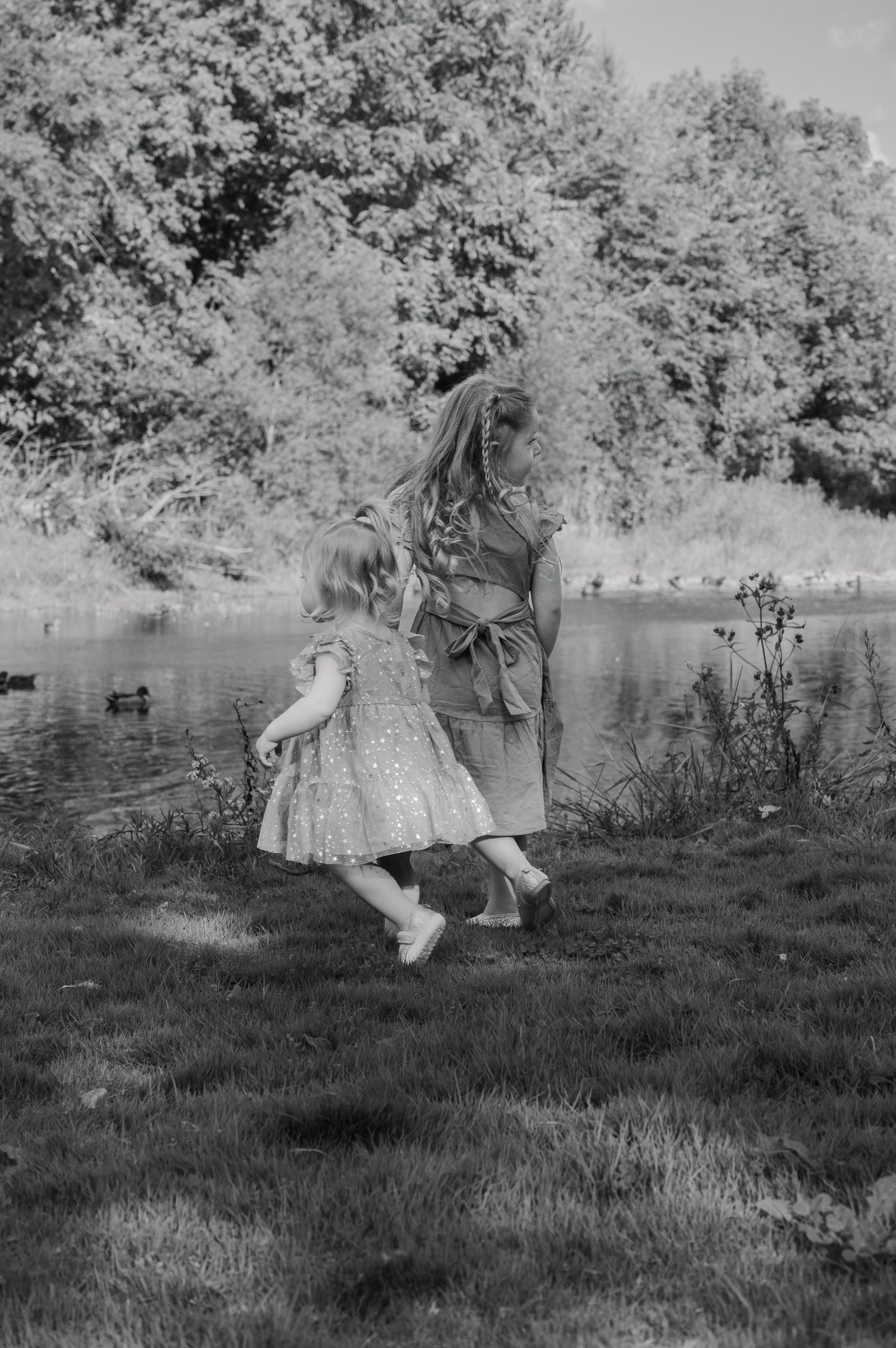Black and white photo of two young sisters walking towards the riverbank.
