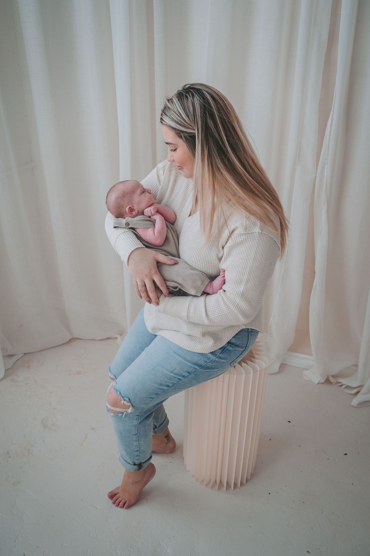Barefoot parent in casual attire holding infant while sitting on decorative white column.