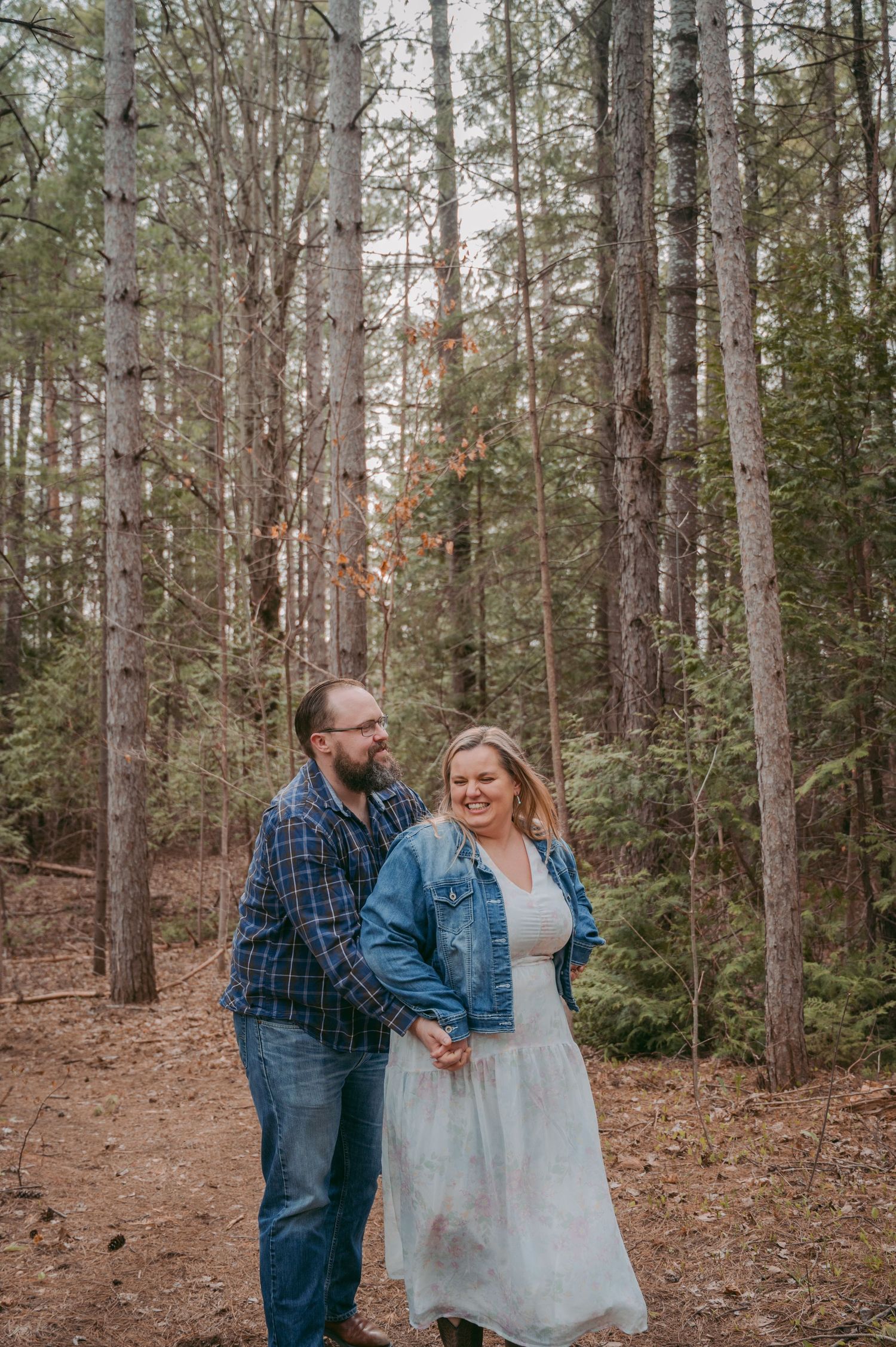 Candid moment of laughter between couple in a wooded setting wearing casual attire.