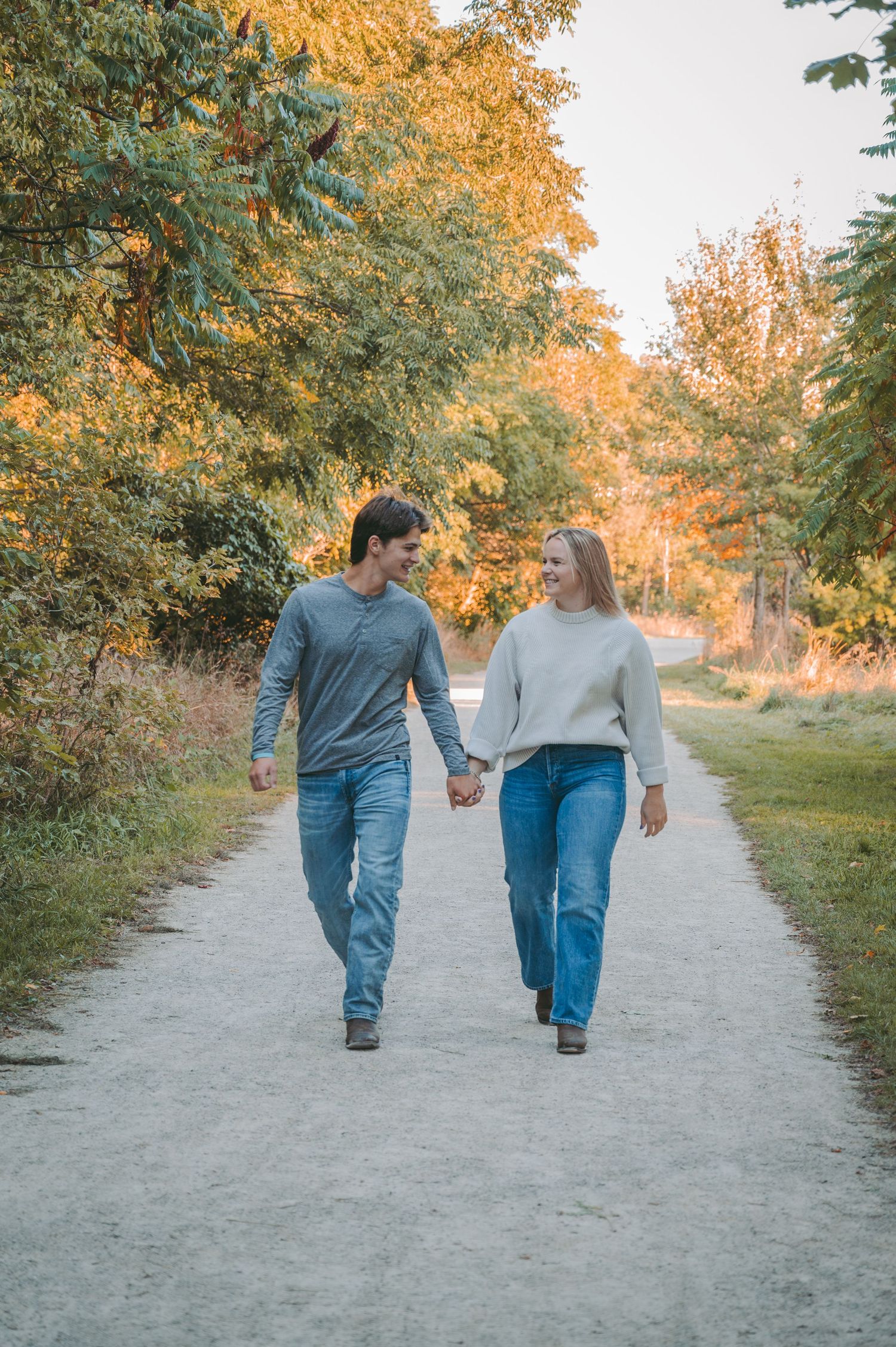 A couple walks hand in hand down a path surrounded by golden autumn foliage.