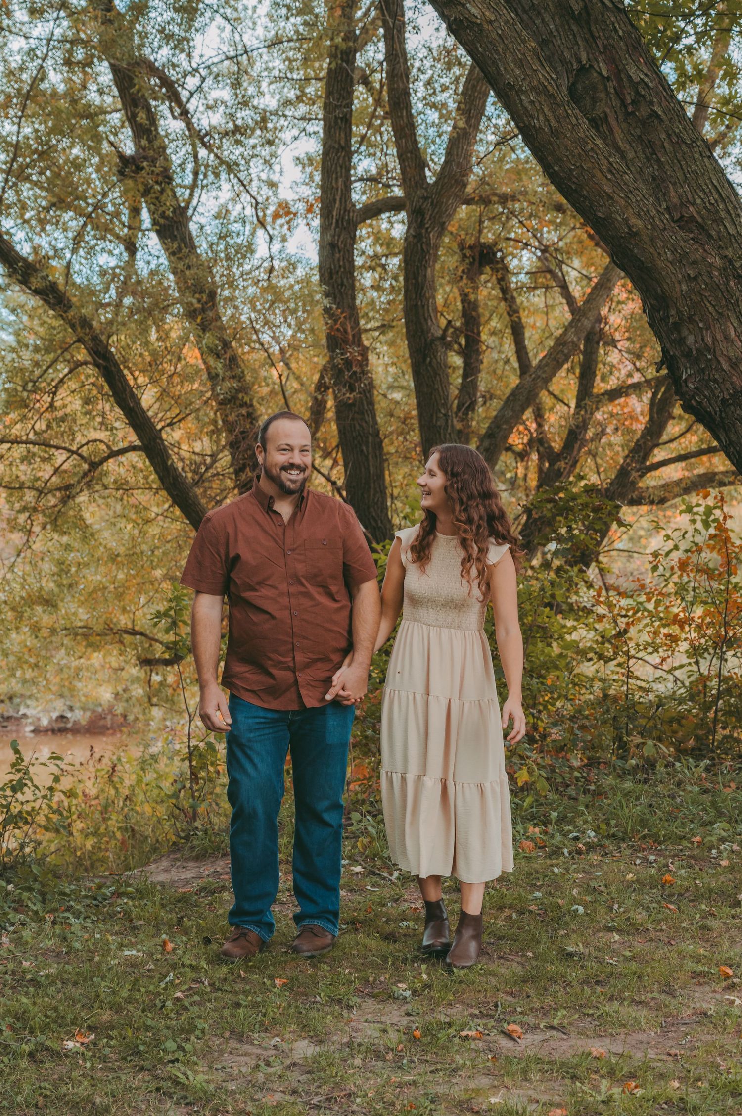 A couple stands together on a woodland path during golden hour.