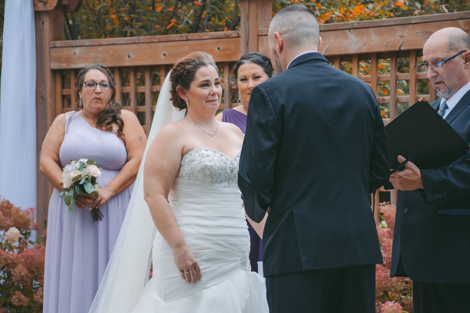 An outdoor wedding ceremony with lattice backdrop and fall foliage.