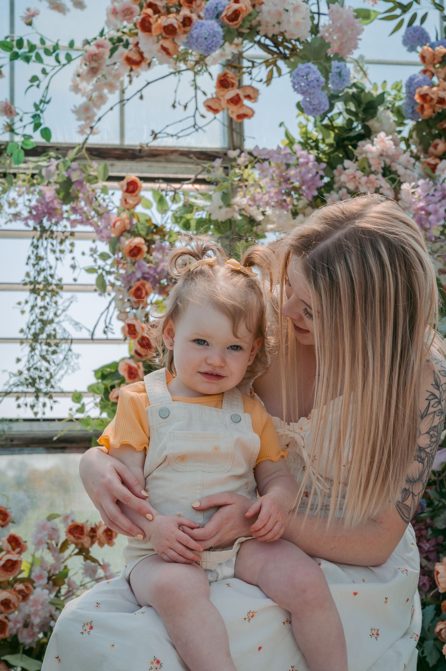 Mother and toddler share sweet moment under floral arch with blooming spring flowers.