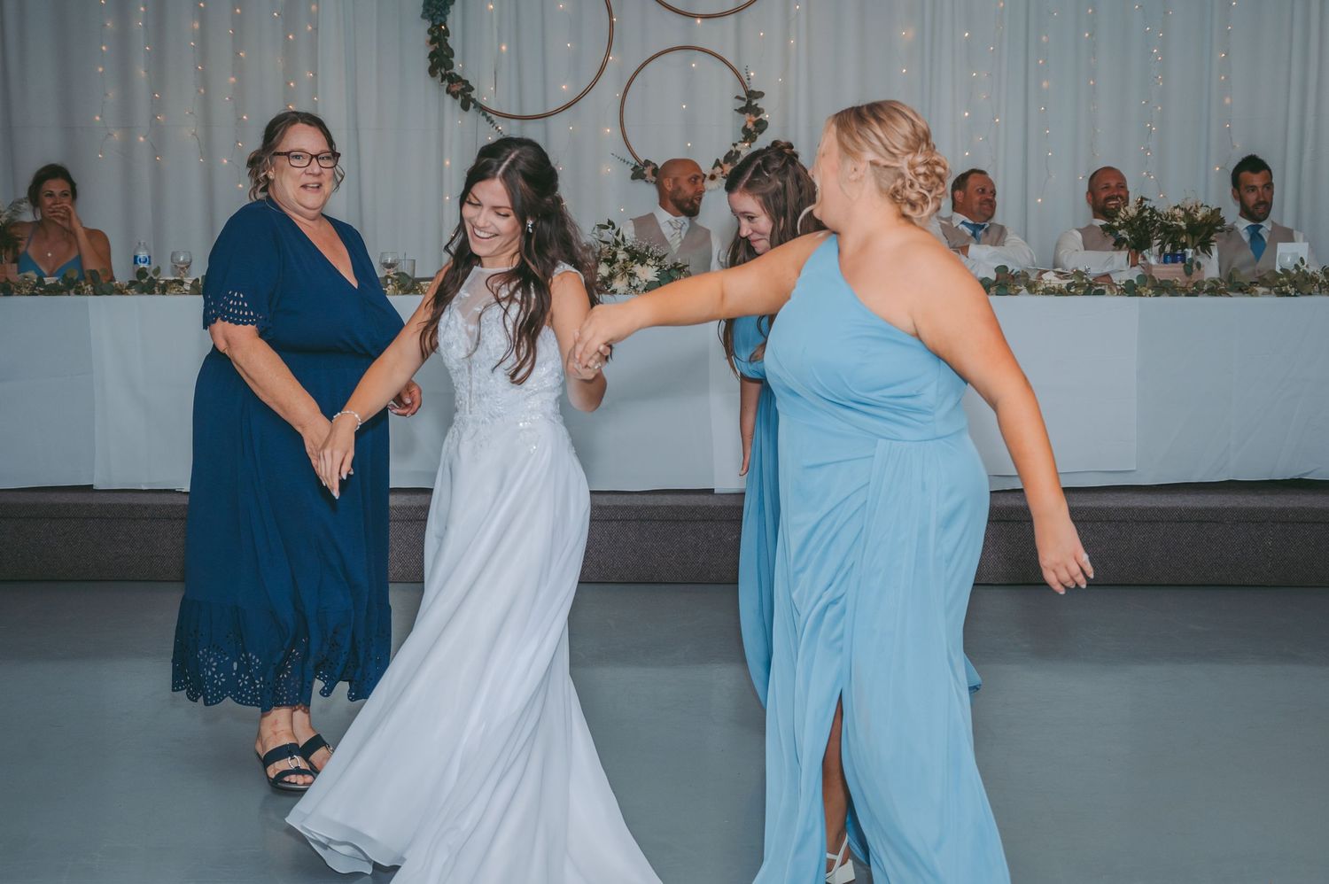Wedding reception dance floor moment with bride and family in blue dresses.