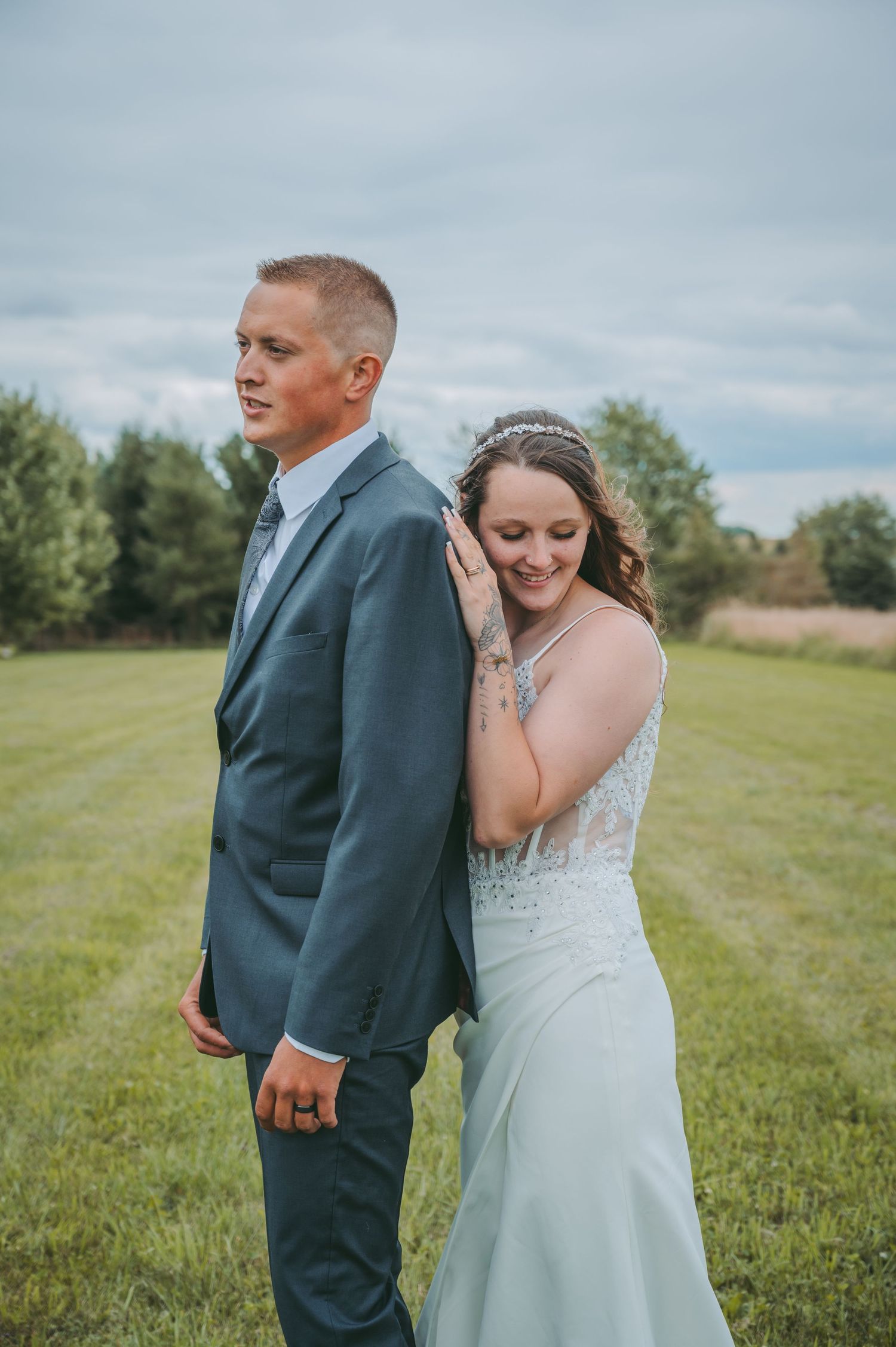 A tender moment between a bride and groom standing in a grassy field under cloudy skies.
