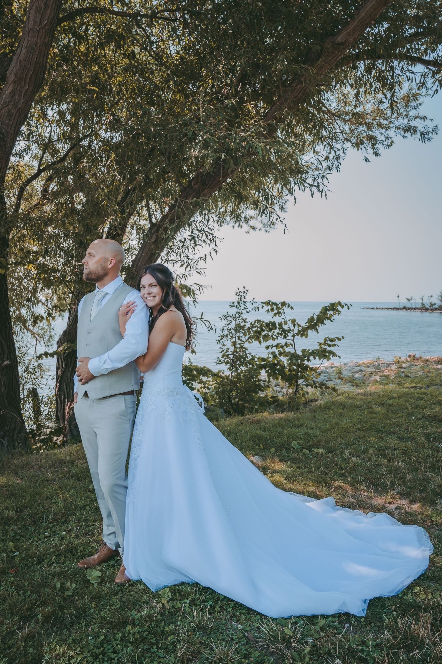 Romantic waterfront wedding portrait with couple standing under a tree by the lake.