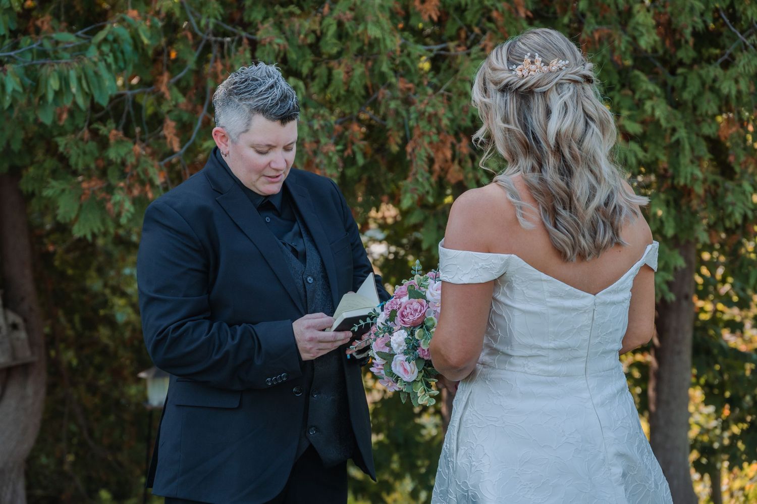 A wedding photo showing a couple exchanging private vows with autumn trees in the background.