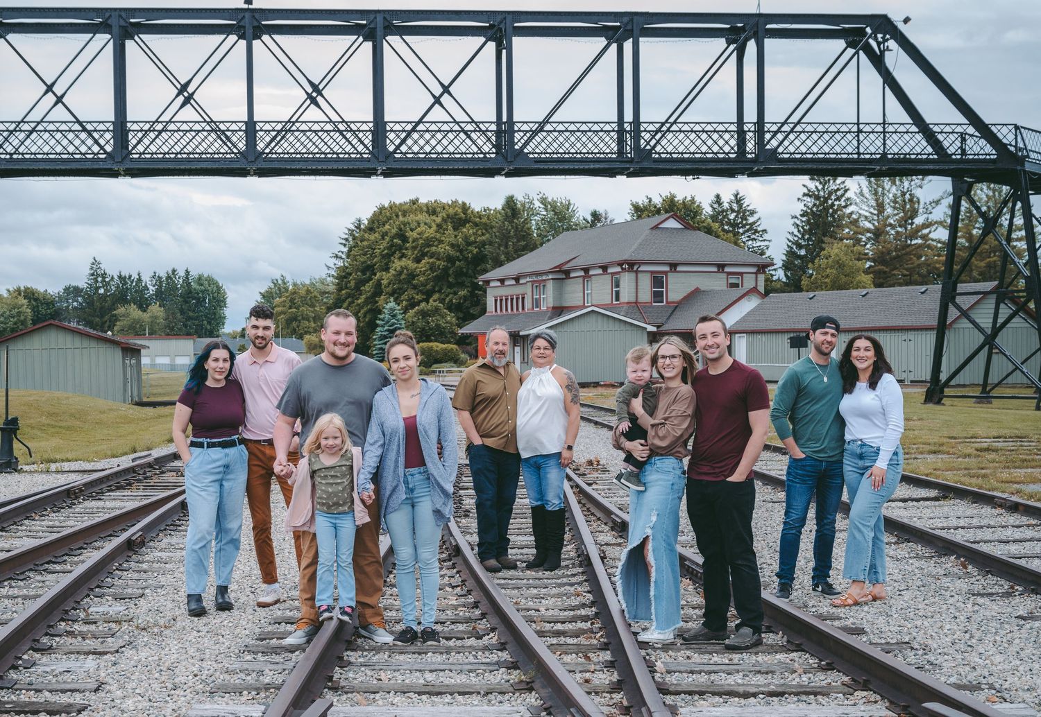 A group of friends gather on railroad tracks with an industrial bridge in the background.