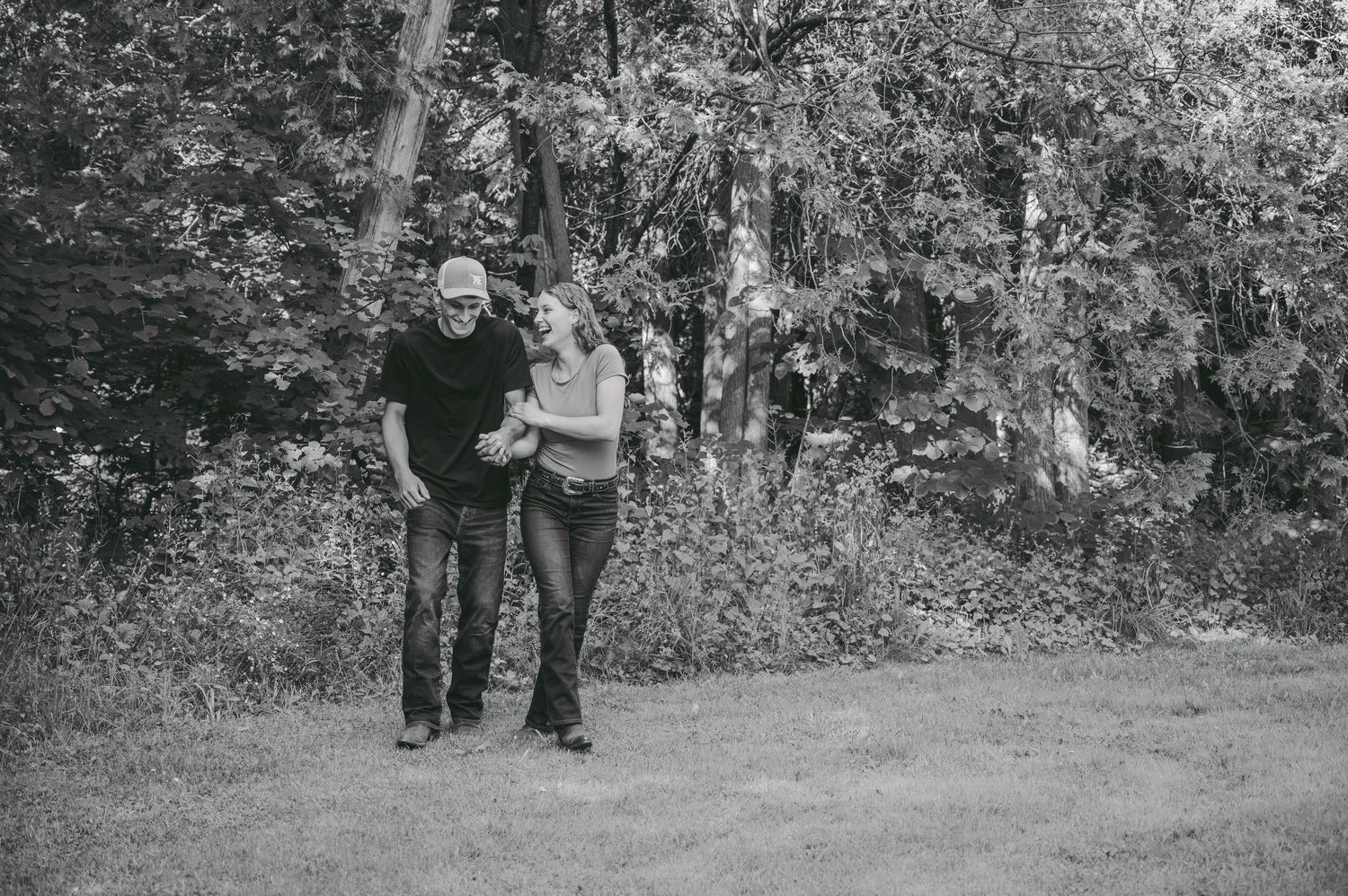 A black and white photo of a couple walking together on a wooded trail.