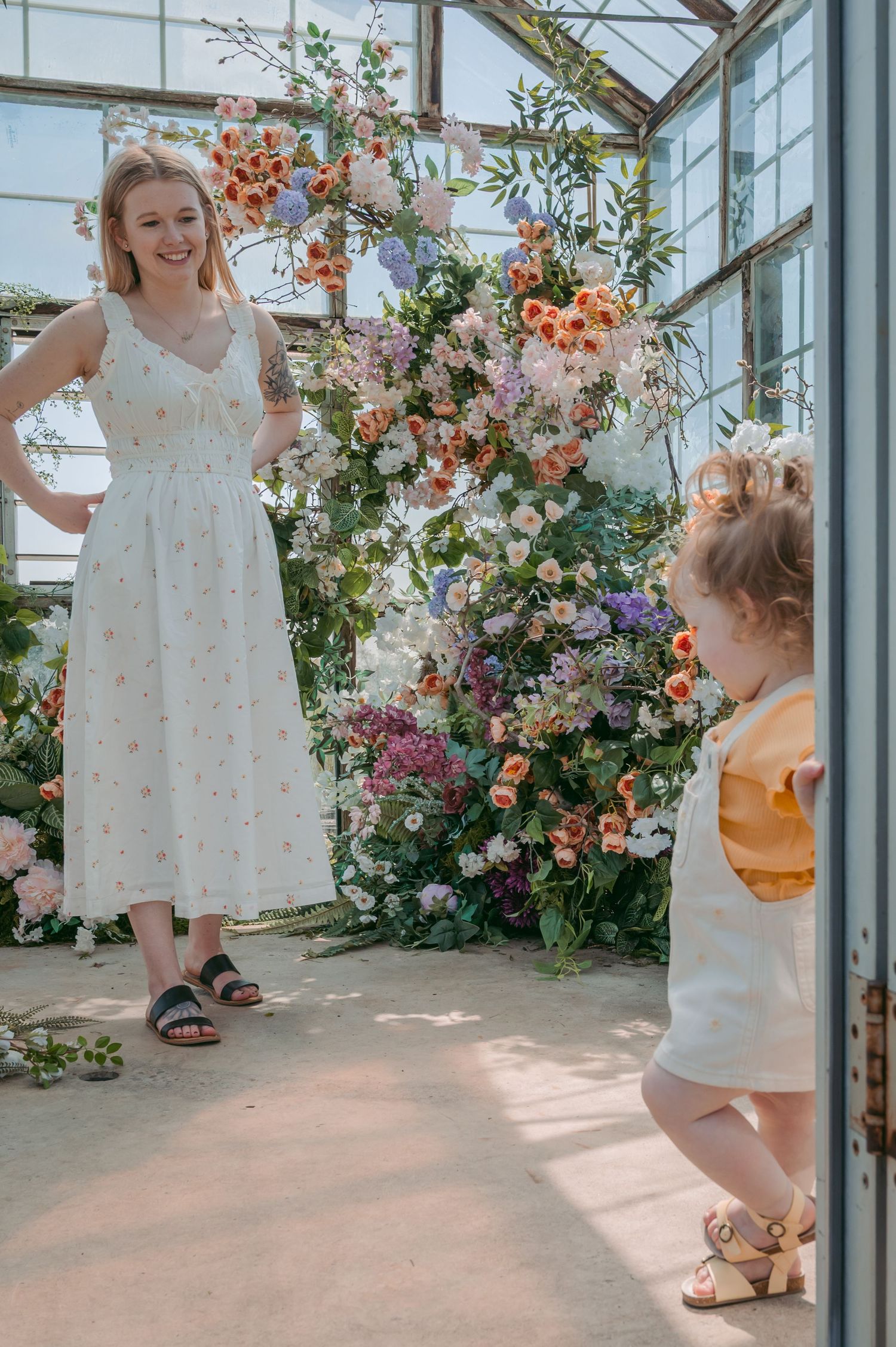 Joyful moment captured in greenhouse with abundant floral arrangements and natural light.
