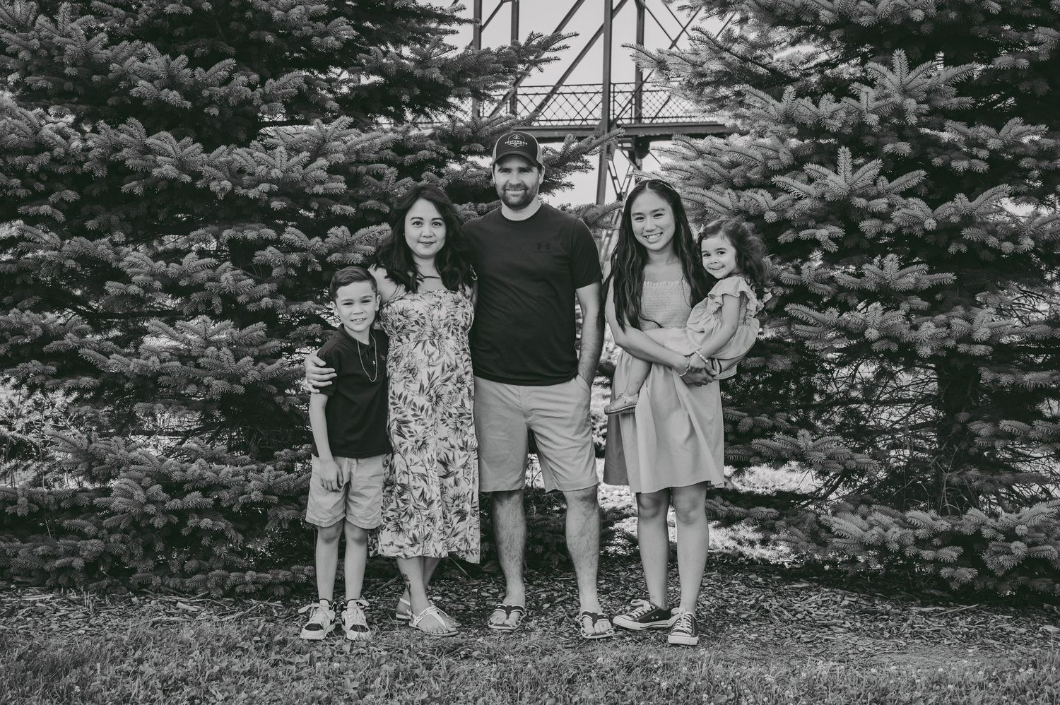 A family portrait session captured against a row of tall evergreen trees.