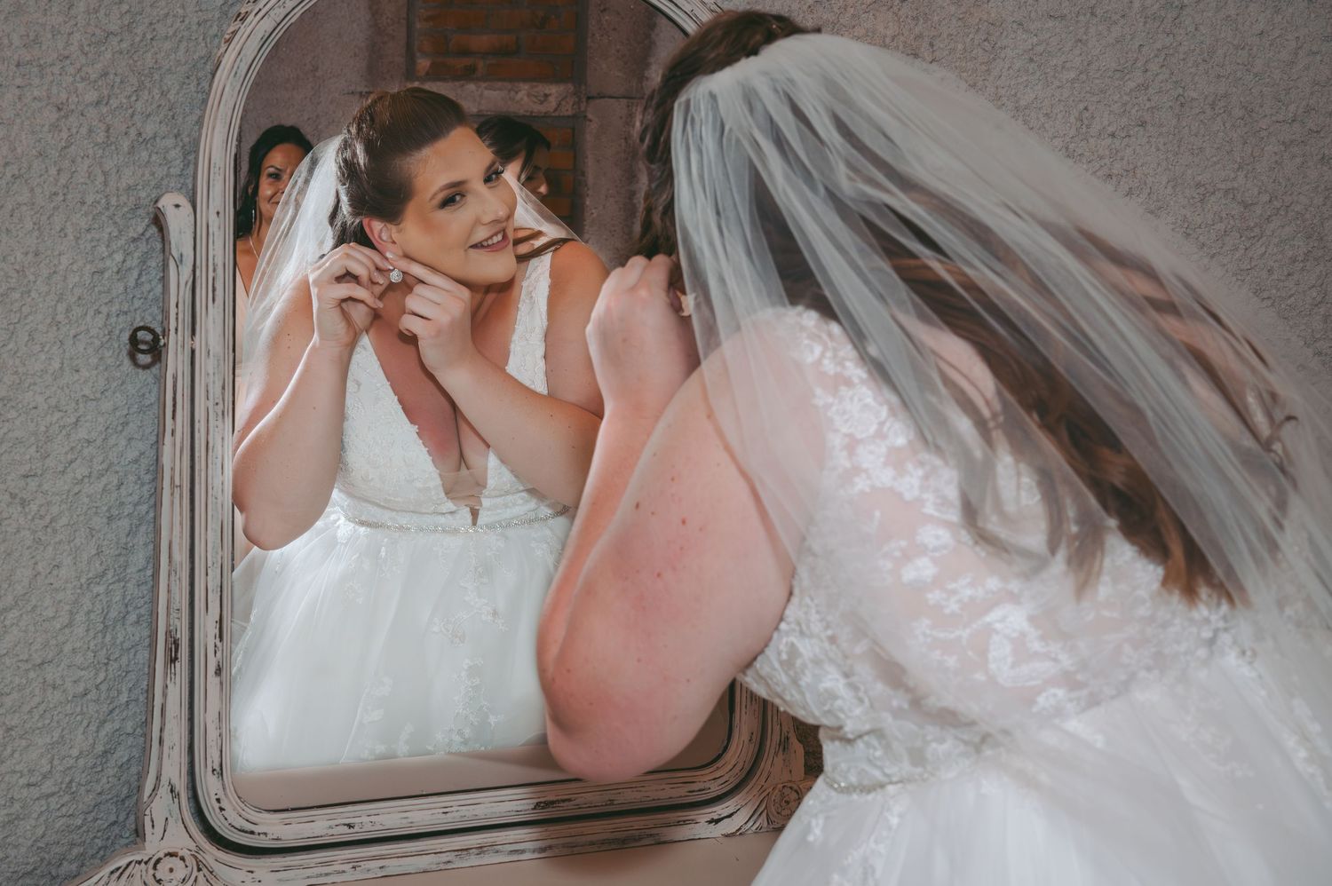 Reflection of getting ready moment in vintage mirror with white wedding dress and veil.