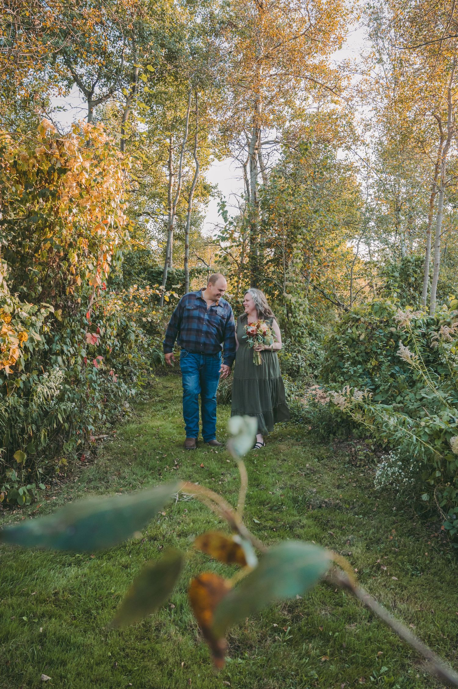 A couple walks hand in hand down a path surrounded by golden autumn foliage.