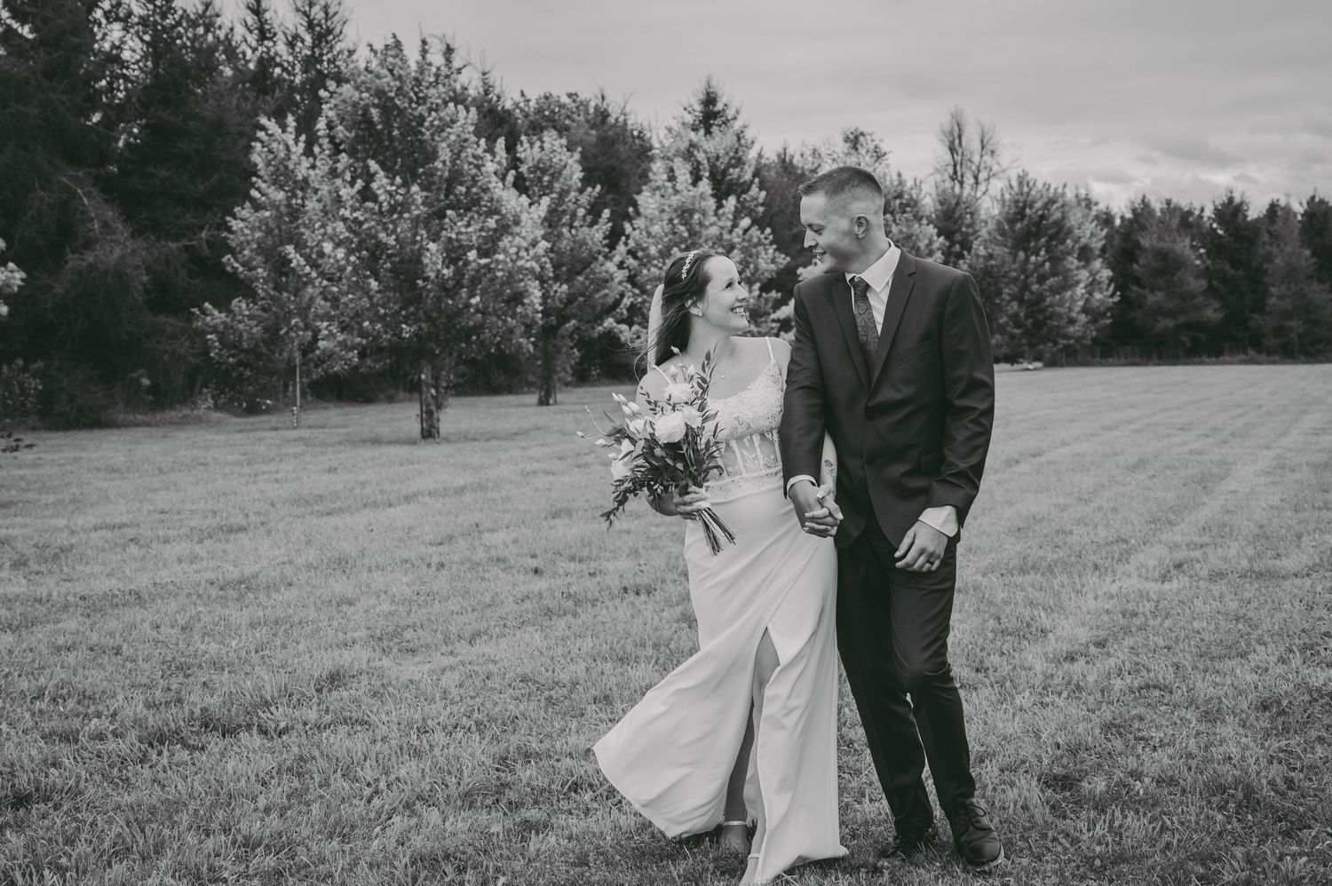 A black and white photo of a couple walking together across a grassy field during their wedding.